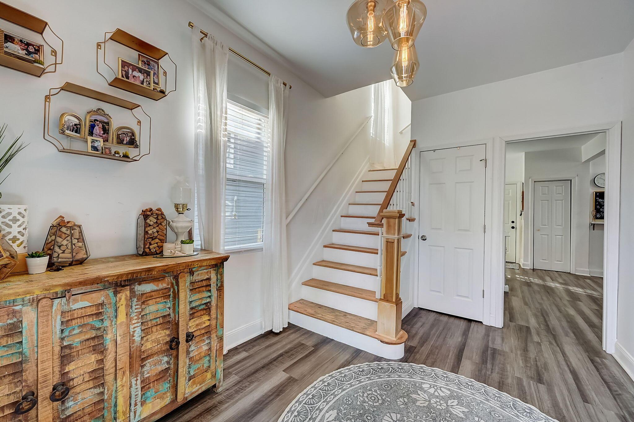 Bright entryway with a white staircase, rustic colorful cabinet, and patterned round rug.