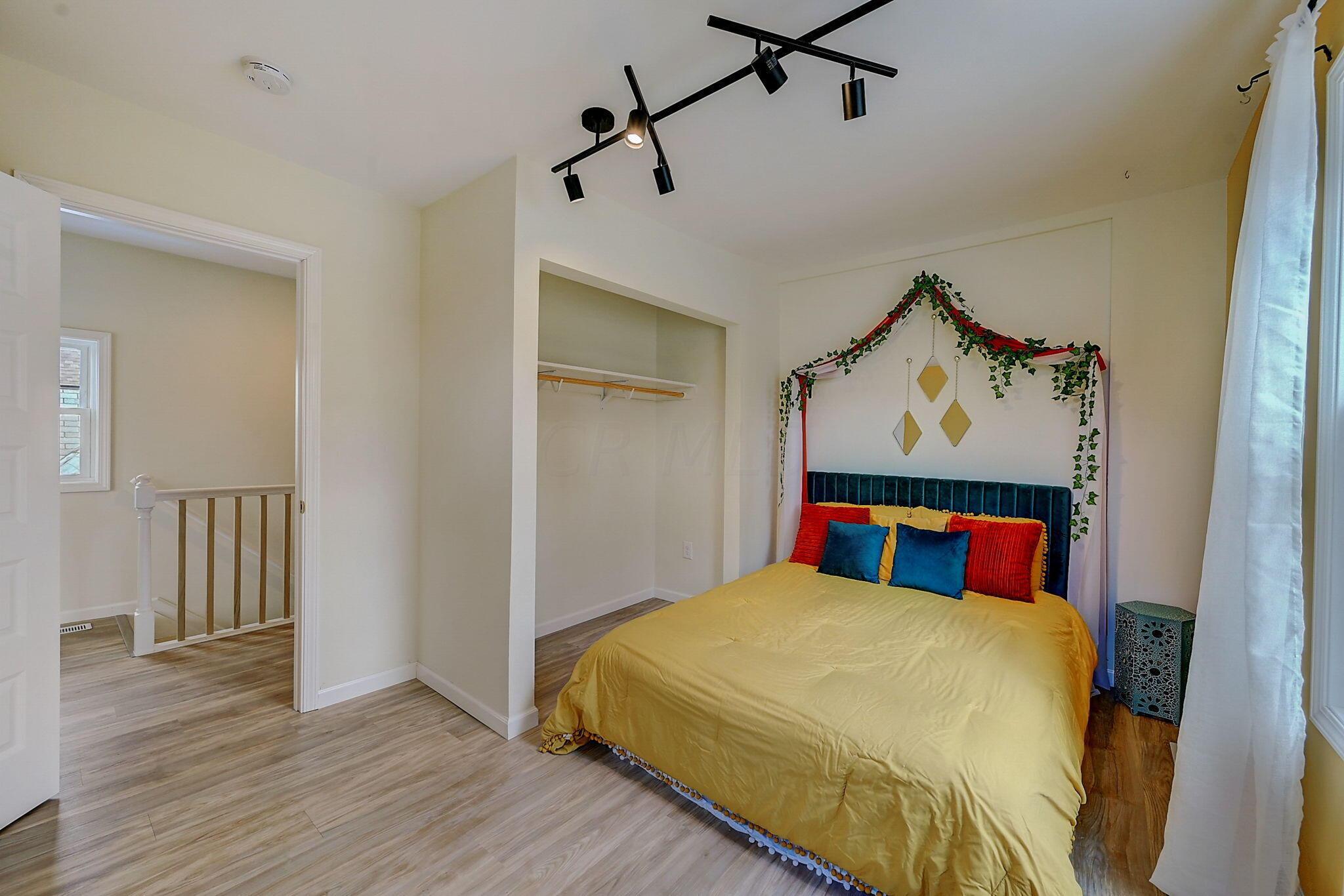 Bedroom with a yellow bedspread, teal headboard, and open closet.