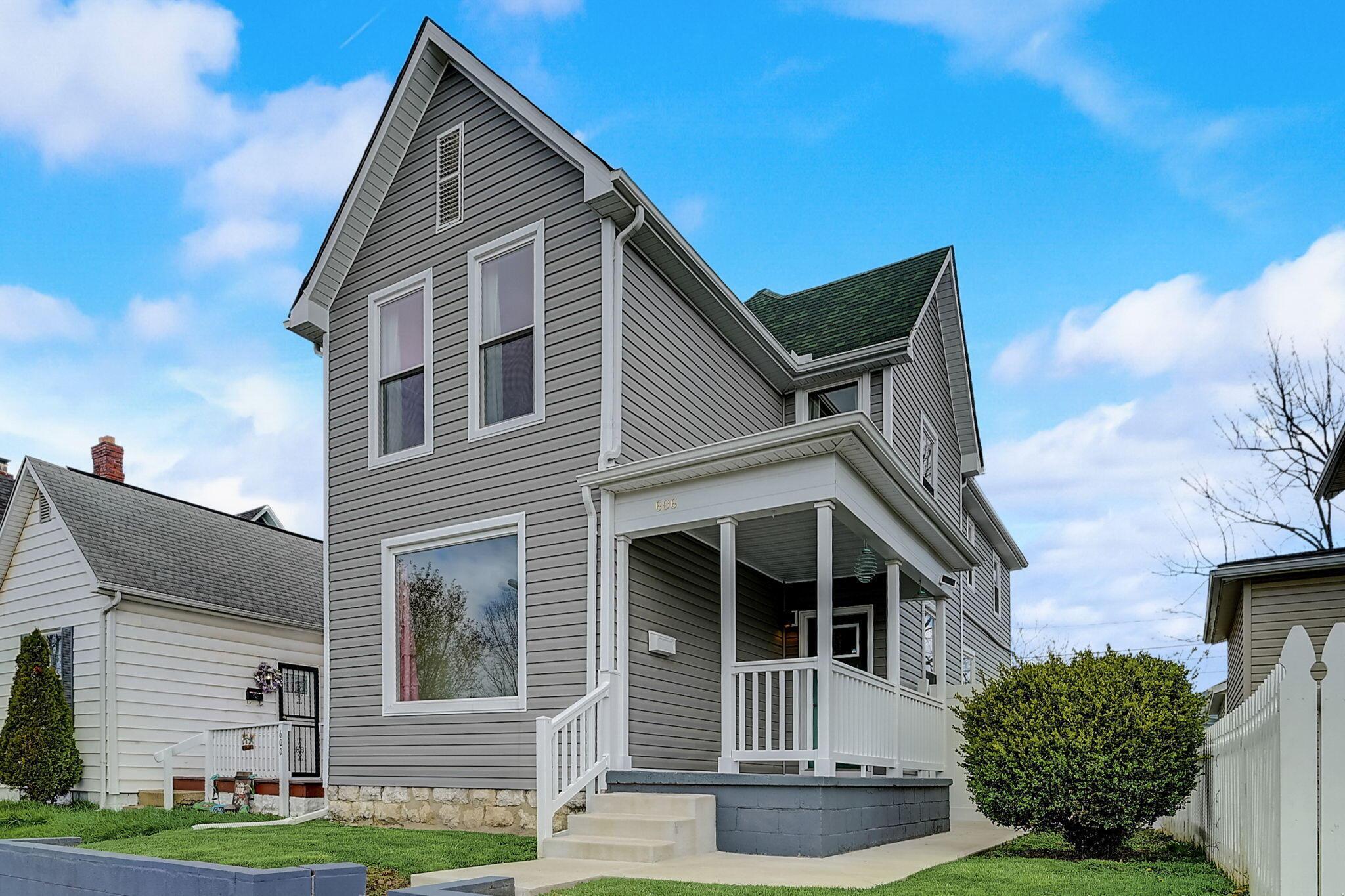 Two-story gray house with a steep gabled roof, white-trimmed porch, and stone foundation.