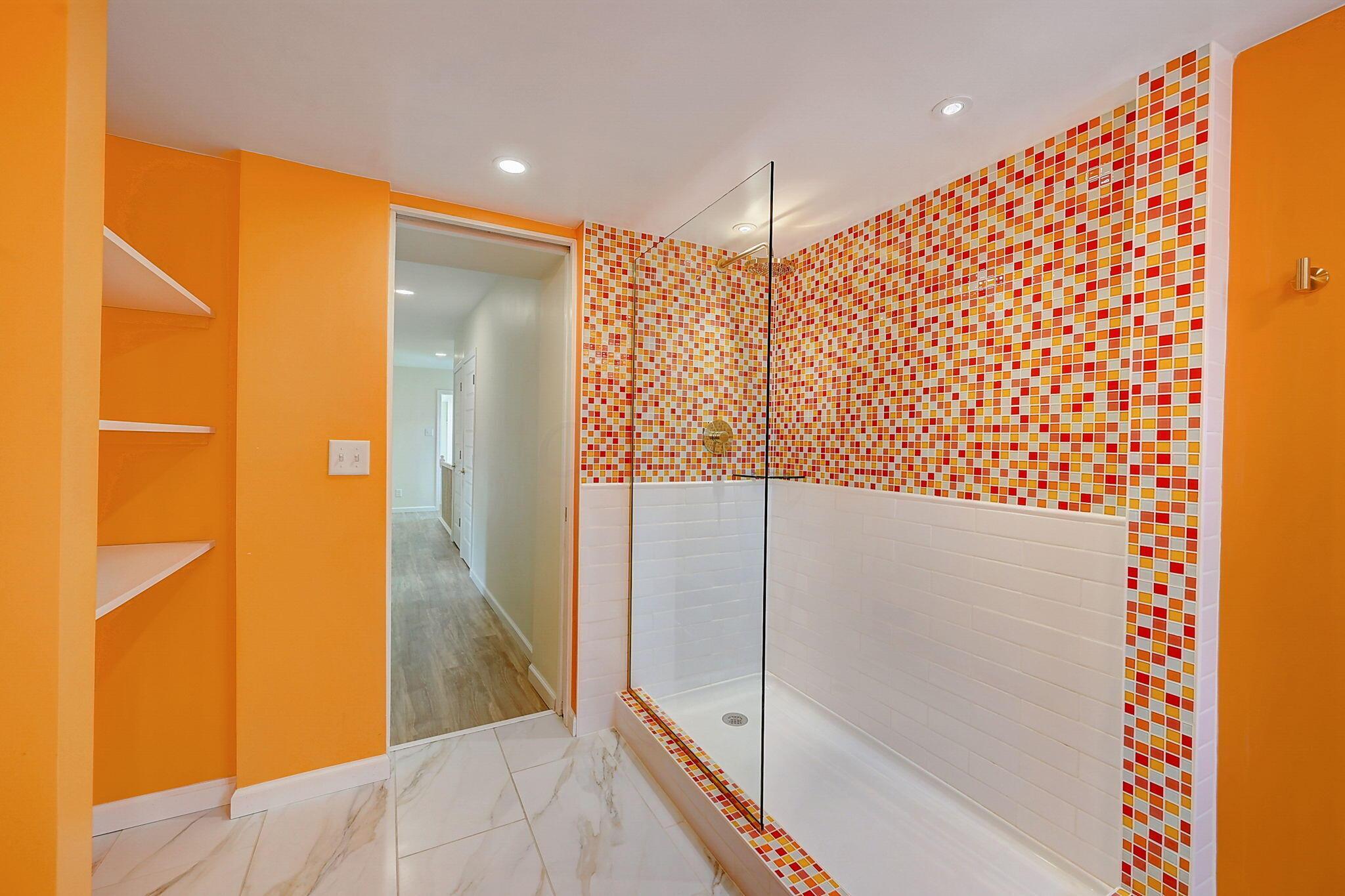 Bathroom with a glass walk-in shower and colorful mosaic tile against bright orange walls.