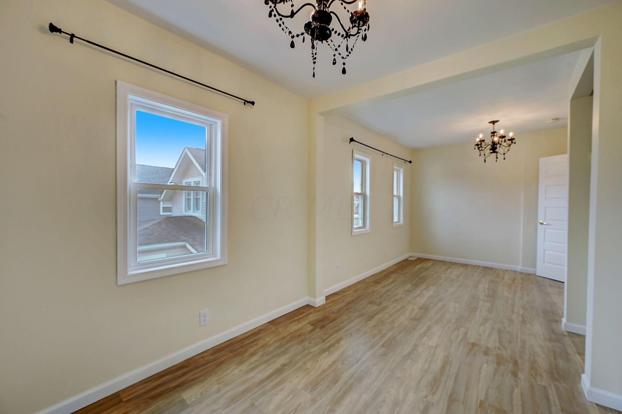 Empty dining room with wood flooring, tall windows, and two chandeliers.