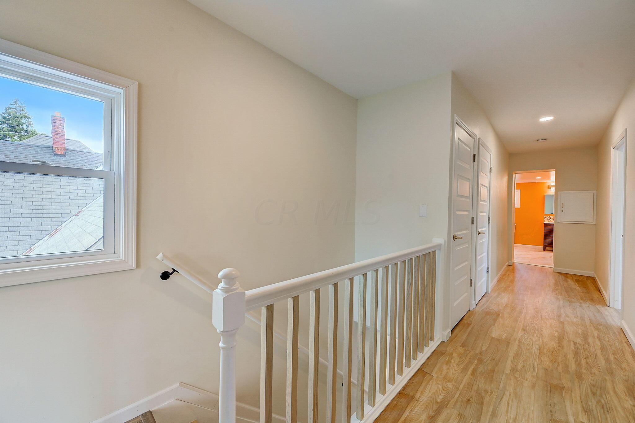 Upstairs hallway with a white stair railing, large window, and orange room visible through the doorway.