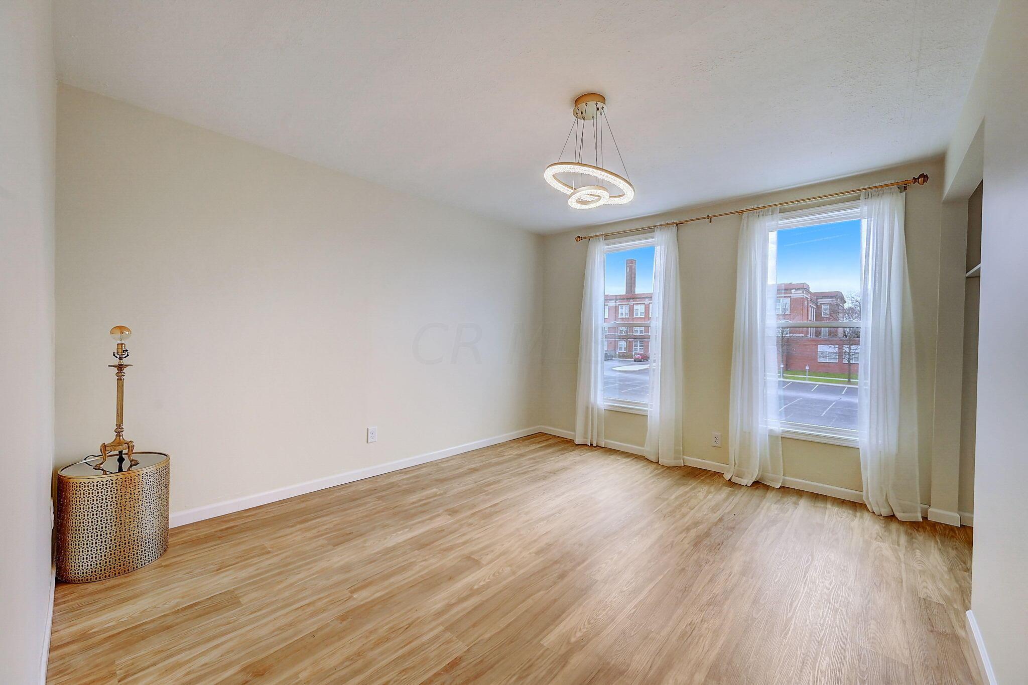 Unfurnished room with light wood floors, two curtained windows, and a circular pendant light.