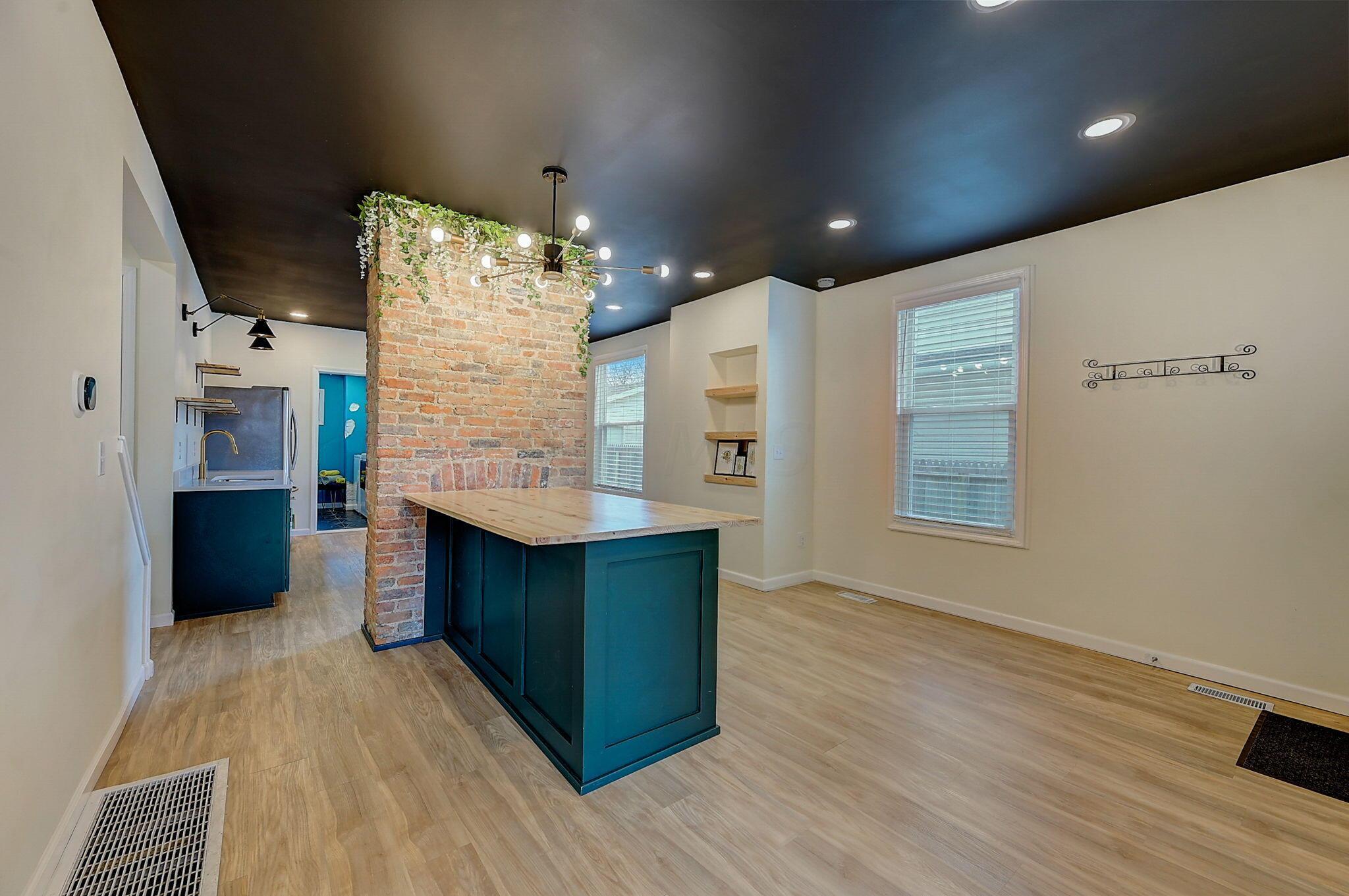 Kitchen and dining area with a teal island, butcher-block countertop, and exposed brick column.