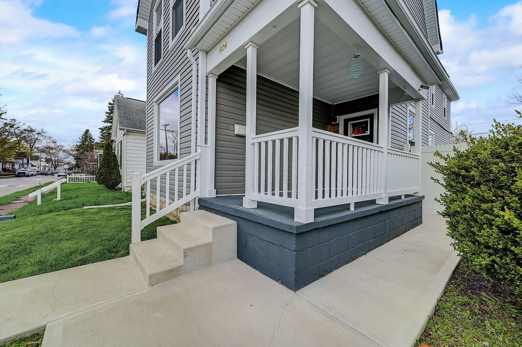 Gray house with a covered front porch, white railings, and concrete steps.