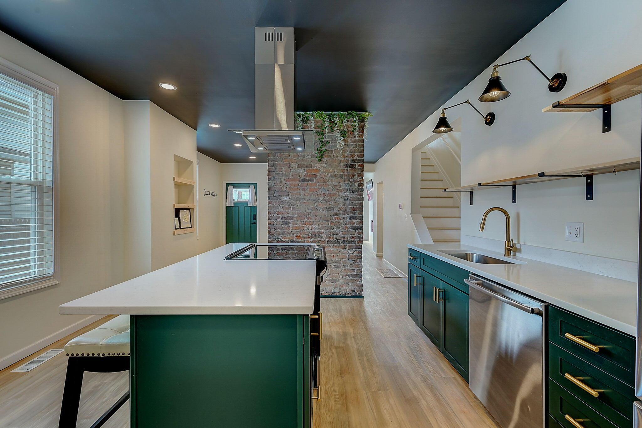Kitchen with green cabinets, a white island, exposed brick, and open wood shelving.