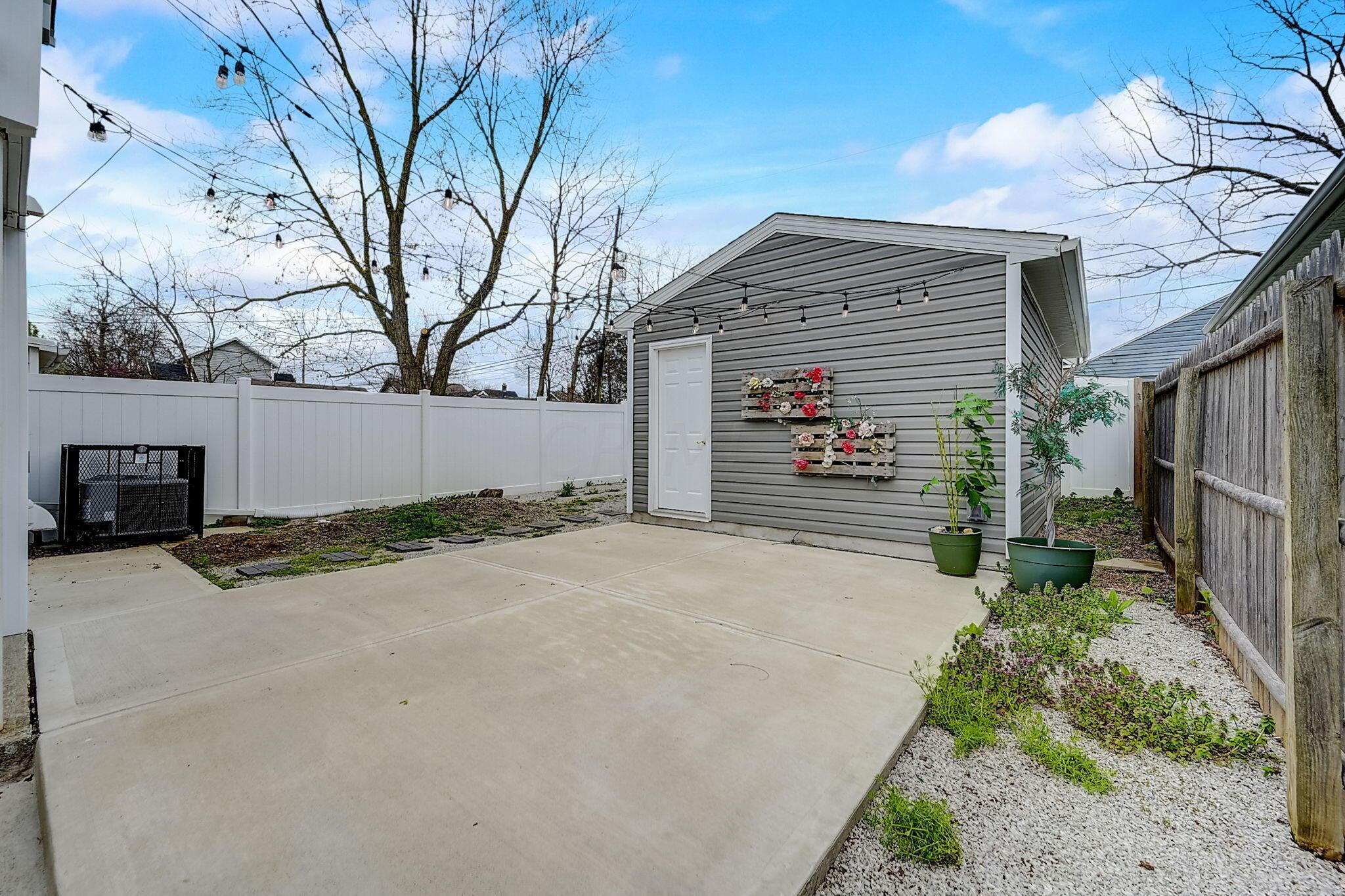 Backyard patio with a gray shed, string lights, and fenced garden beds.
