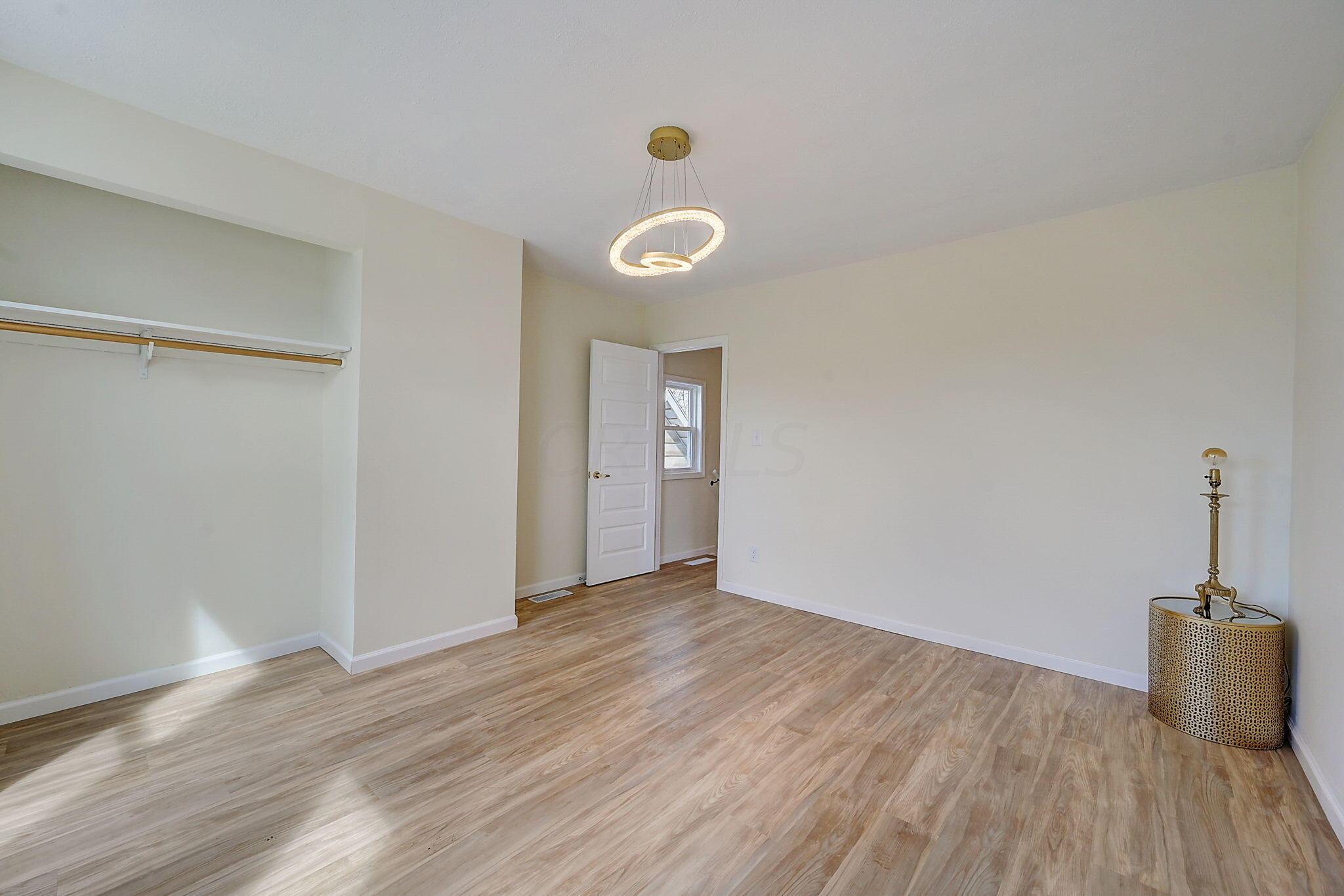 Empty room with light wood floors, an open closet, and a modern circular pendant light.