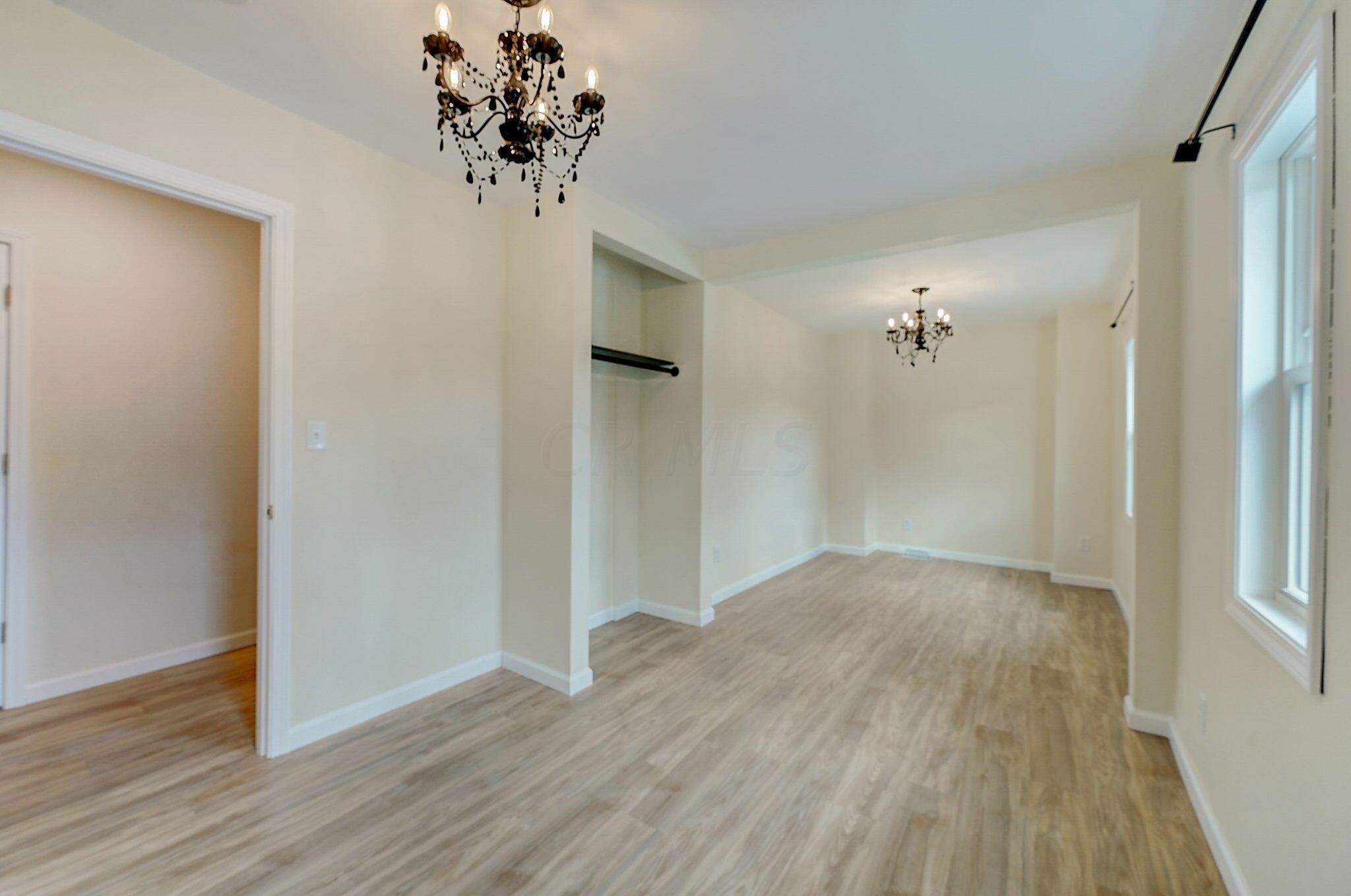 Empty room with wood-look flooring, a closet alcove, tall windows, and two chandeliers.