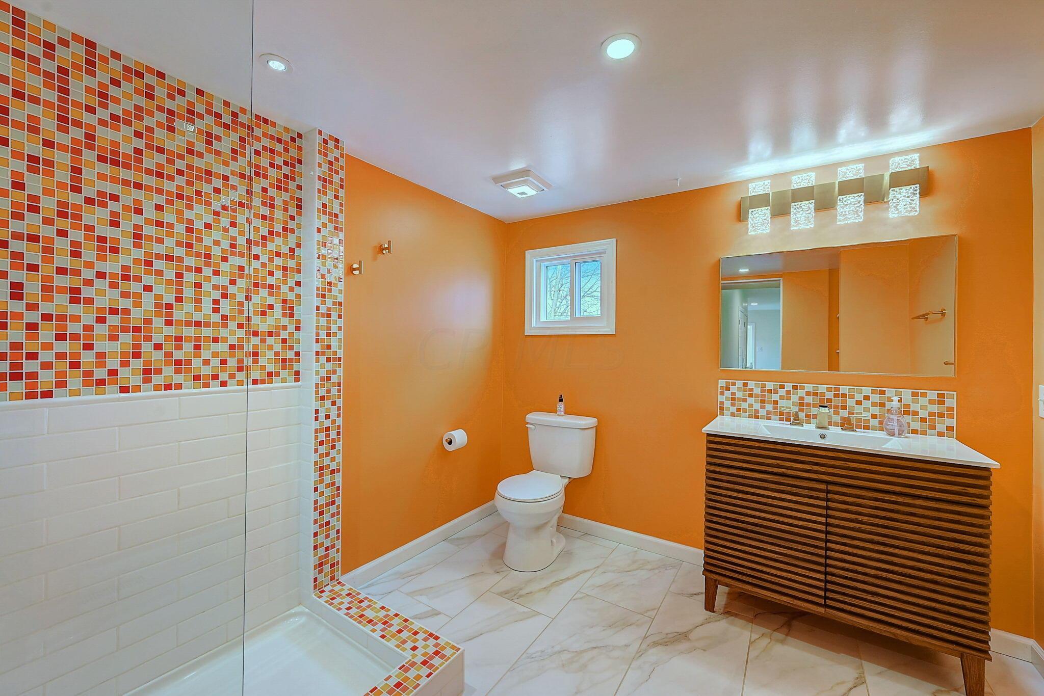 Bathroom with orange walls, multicolored mosaic shower tile, and a dark wood-slat vanity.