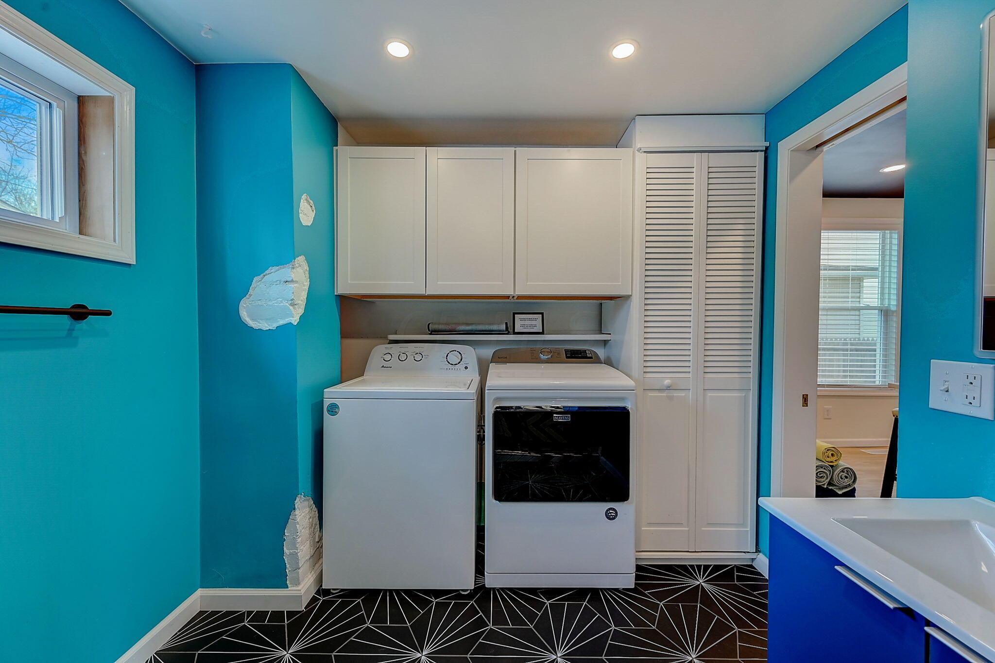 Laundry room with washer and dryer, white cabinets, teal walls, and visible wall damage.