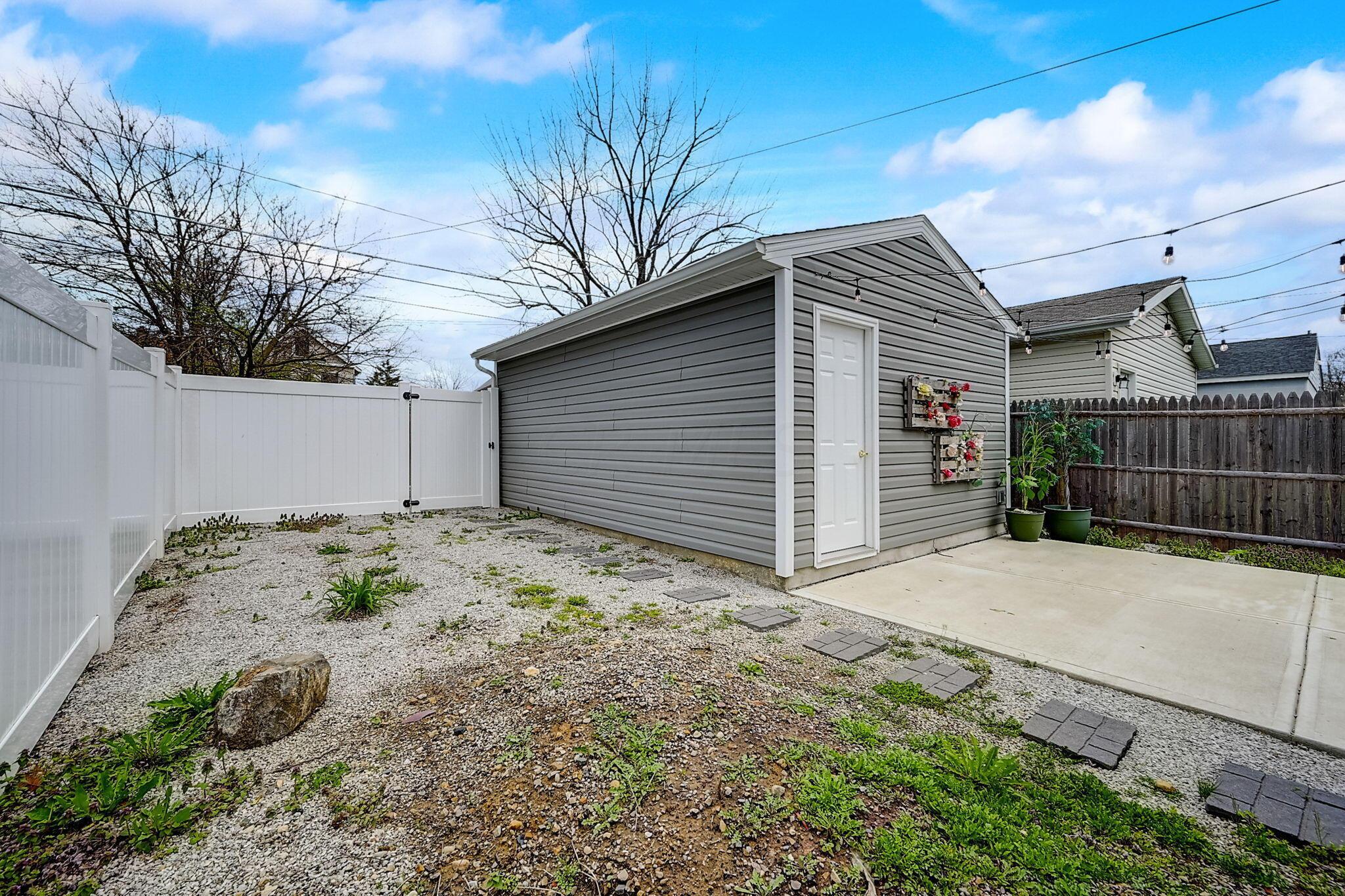 Fenced backyard with a gray storage shed, gravel landscaping, and concrete patio.