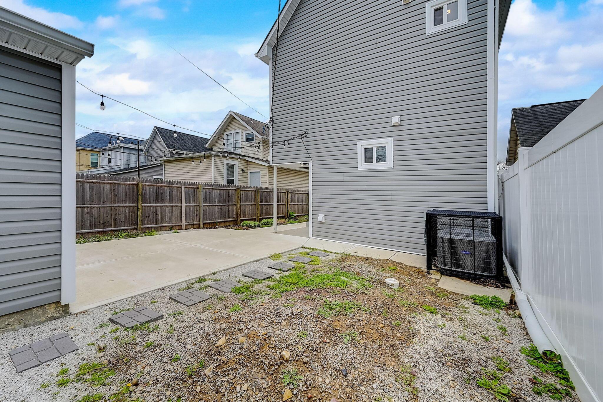 Side yard with a concrete patio, gravel, stepping stones, and fenced boundaries beside a gray house.