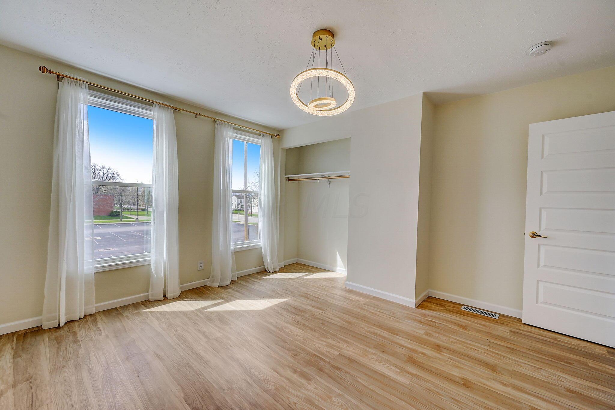 Empty room with light wood floors, two tall curtained windows, an open closet, and a circular pendant light.