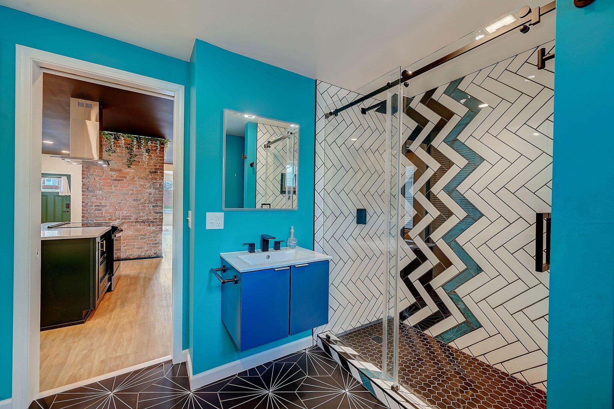 Bathroom with a glass shower, geometric tile accent, blue vanity, and turquoise walls.