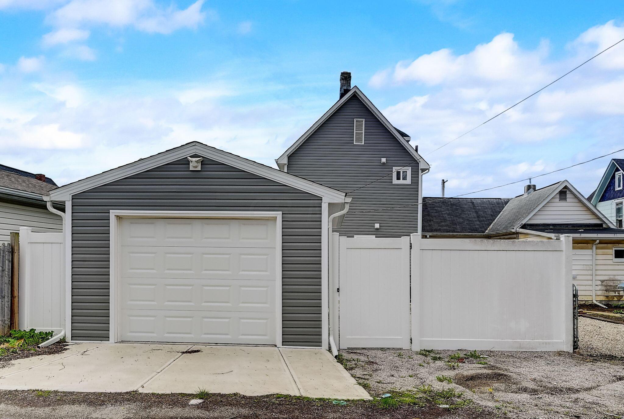 Gray detached garage with a white overhead door and privacy fence in front of the house.