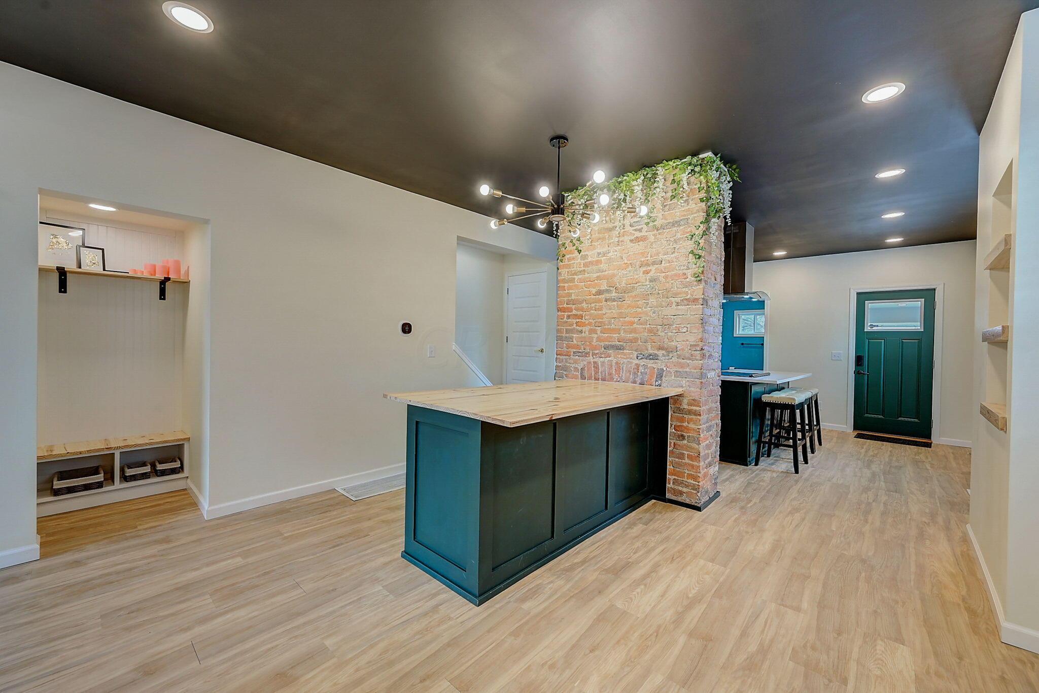Kitchen with a dark teal island, exposed brick pillar, and green entry door.