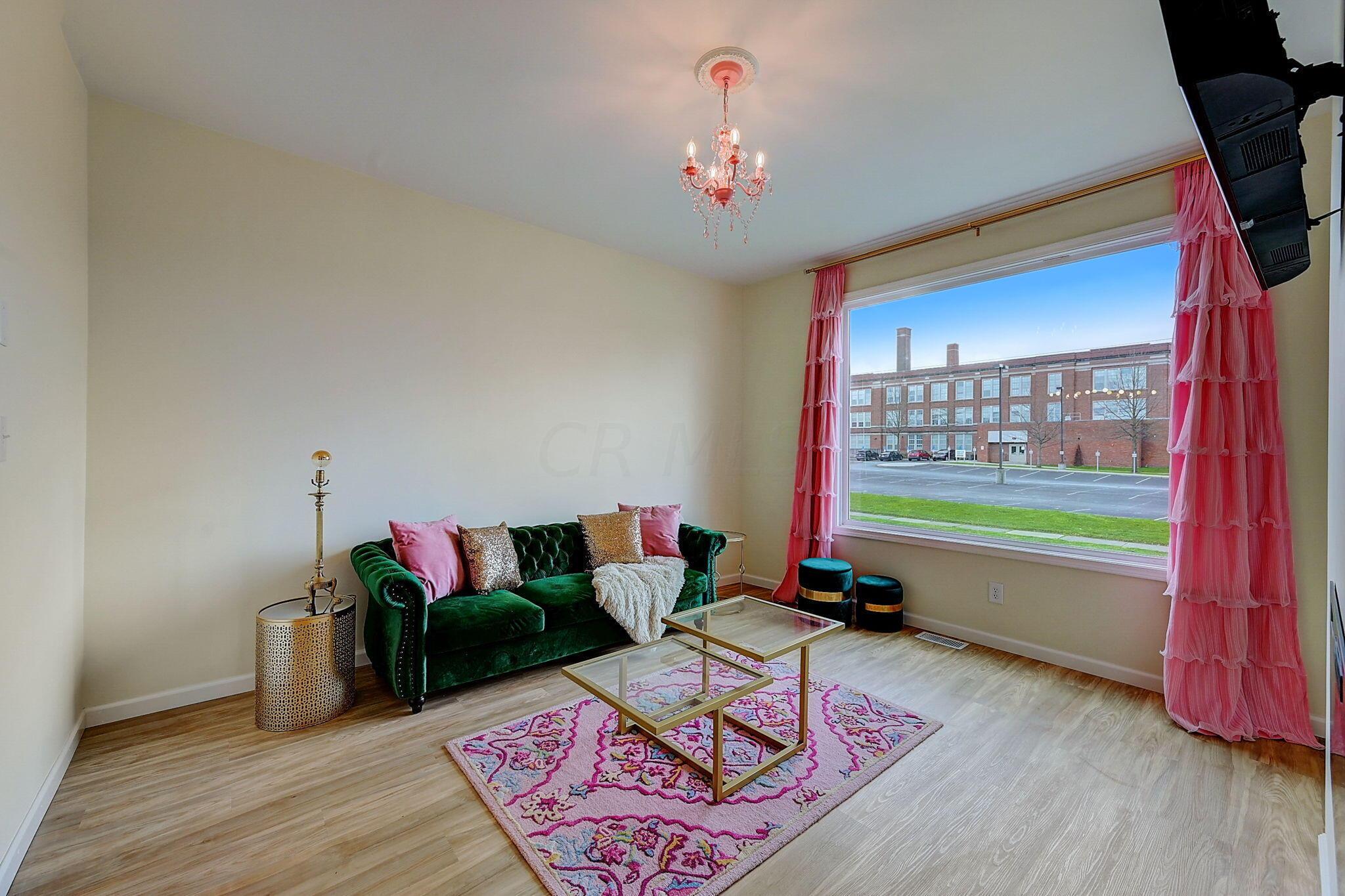 Living room with a green velvet sofa, pink curtains, chandelier, and large window.