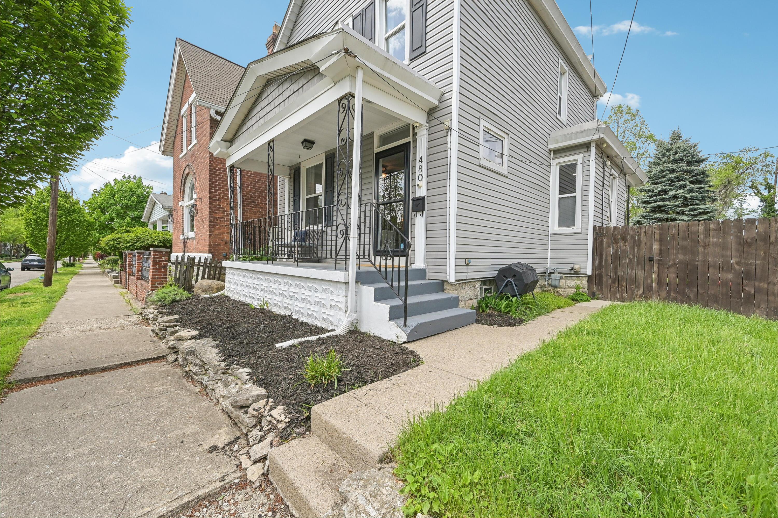 Gray-sided two-story home with a covered porch, black railing, and landscaped yard.