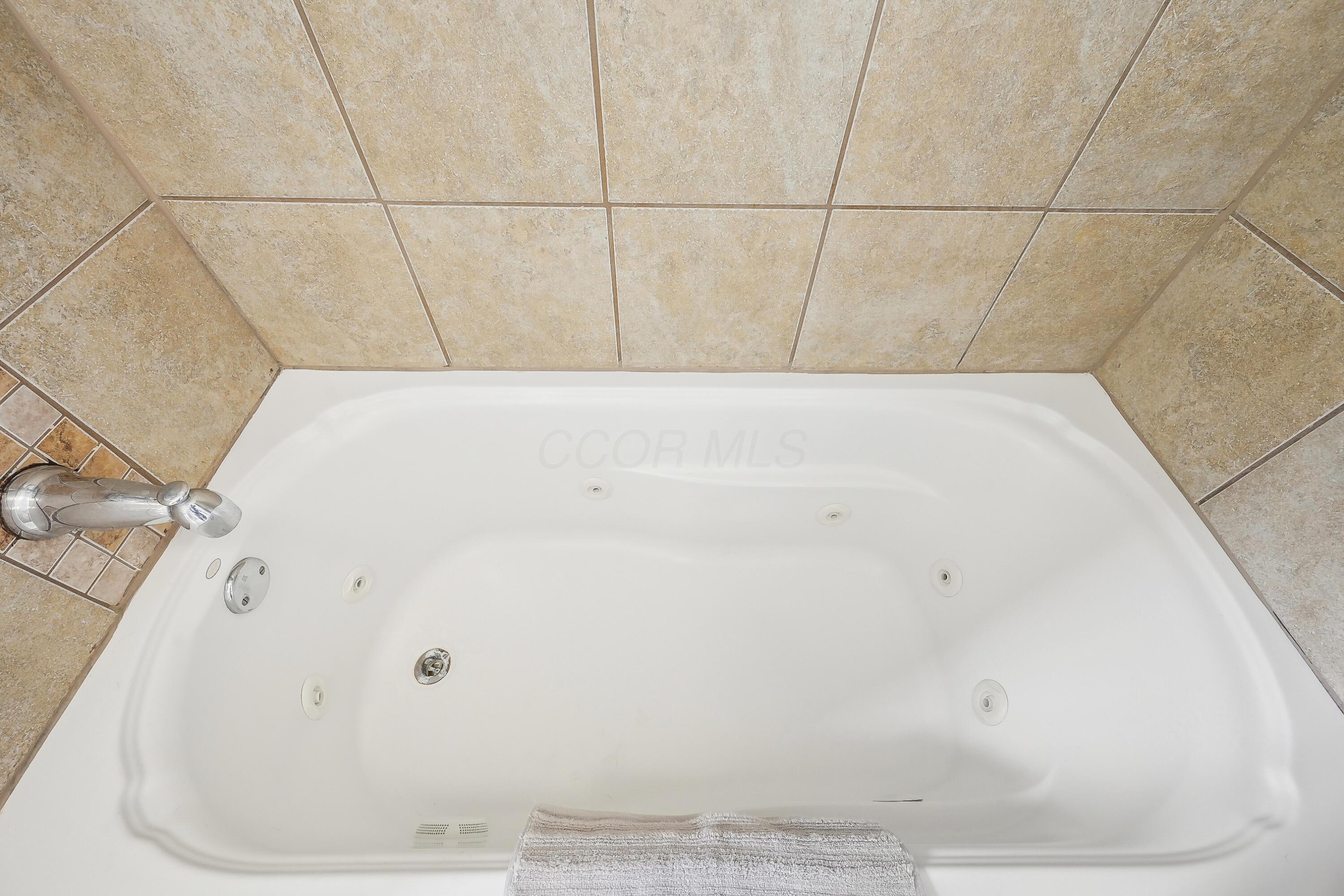 White jetted bathtub with chrome faucet and tan tile surround.