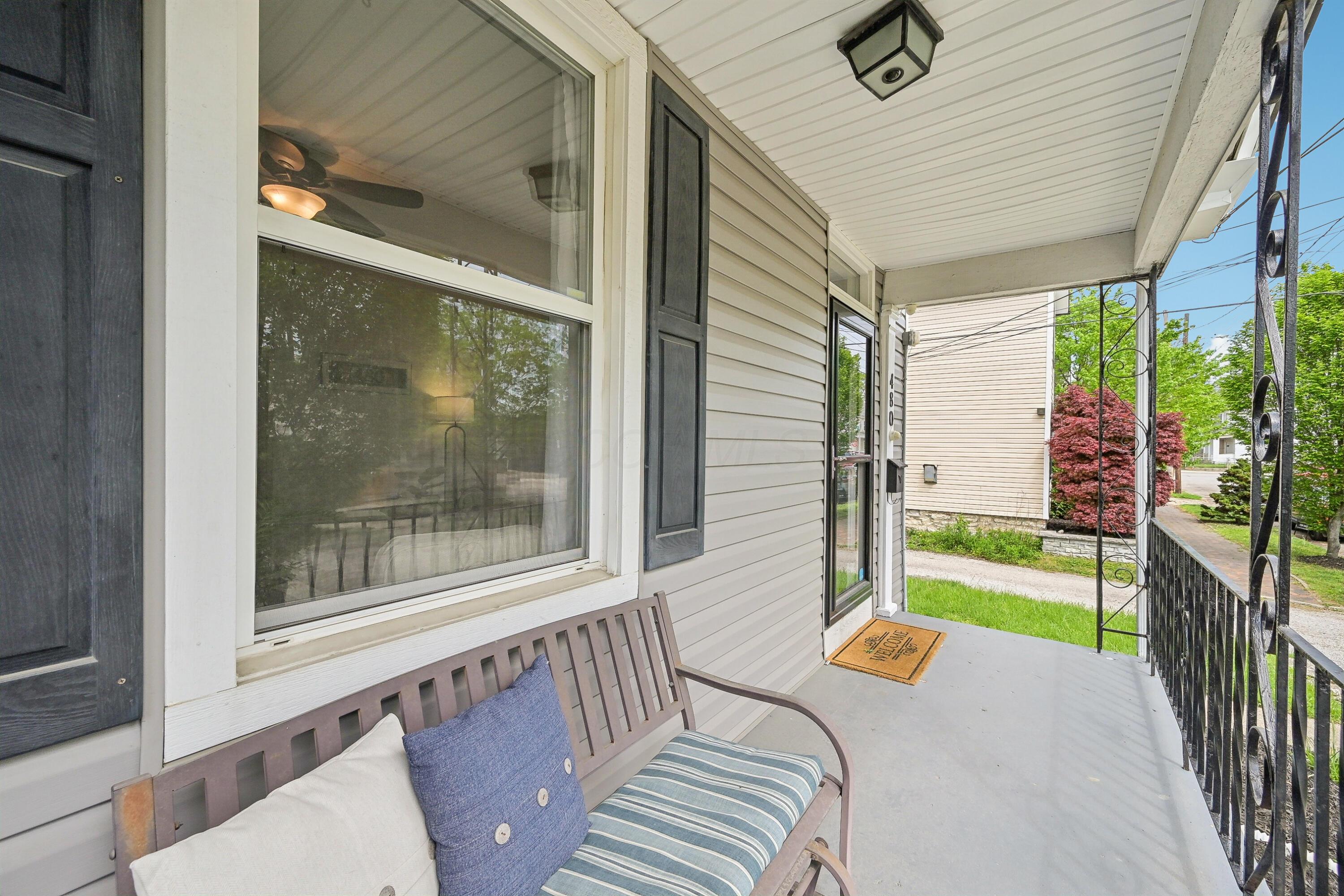 Covered front porch with a cushioned bench, black shutters, and decorative metal railing.