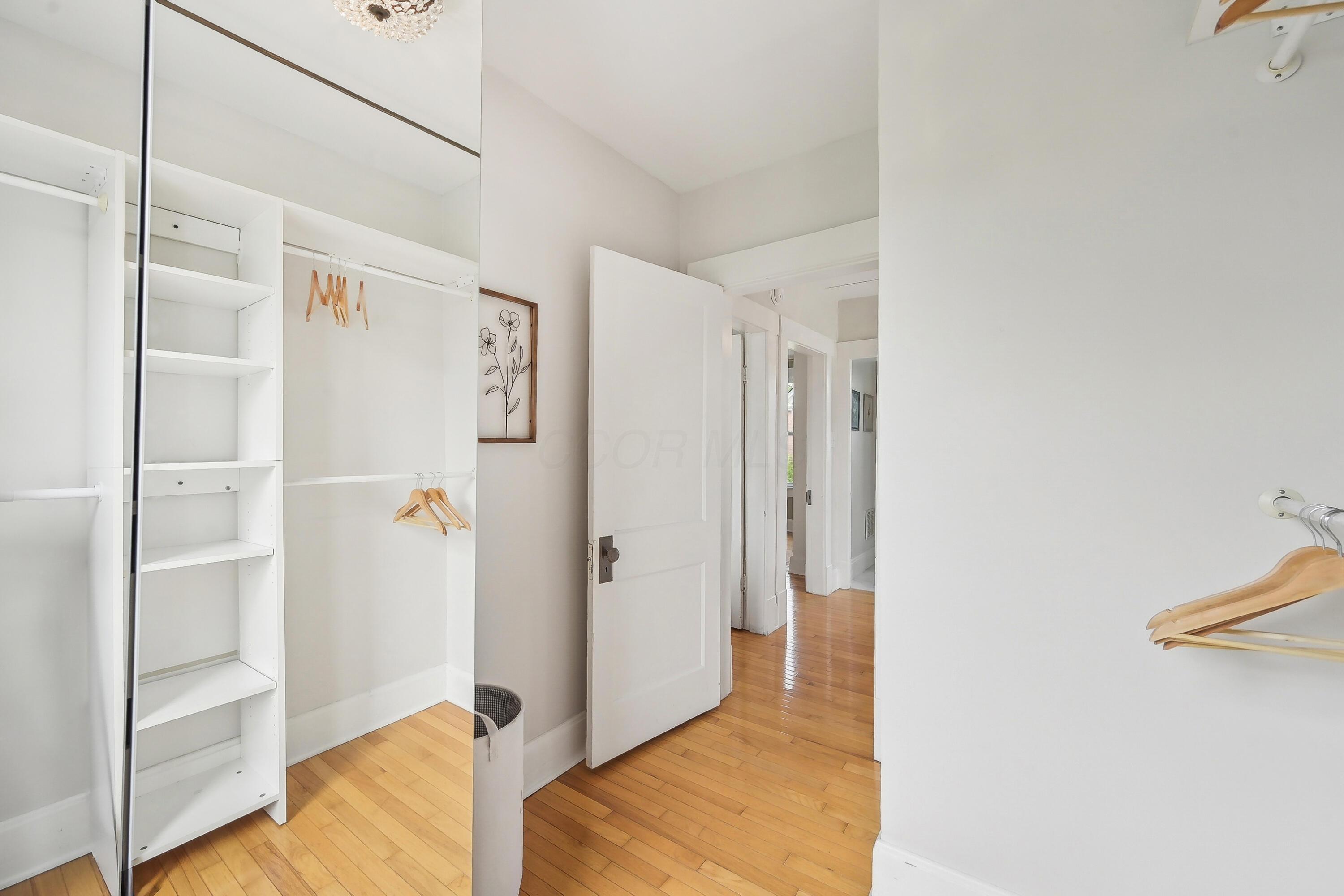 Walk-in closet with white shelving and wooden hangers beside an open doorway to a hardwood hallway.