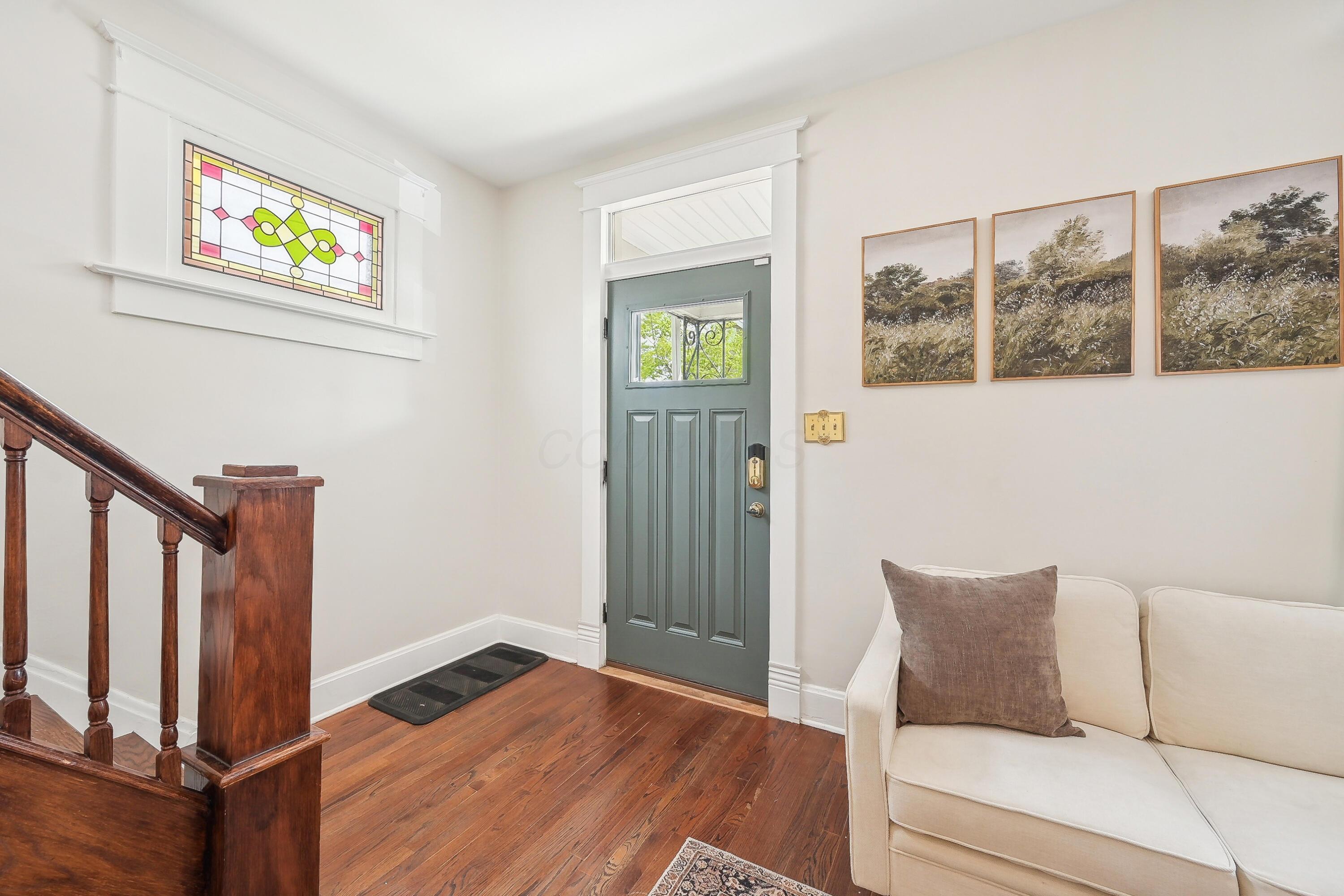 Entry foyer with a green front door, stained-glass transom, hardwood floors, and dark wood staircase.