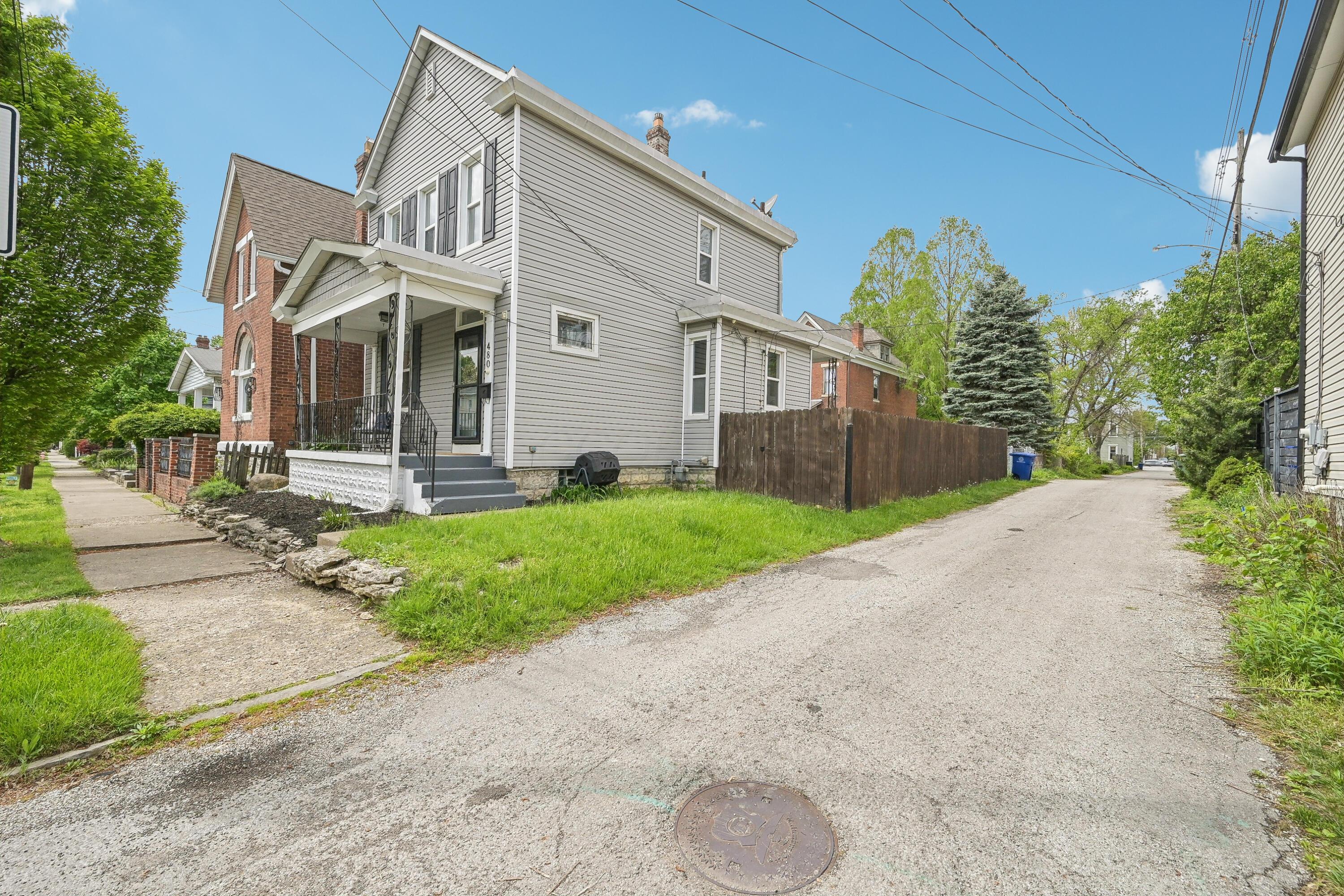Gray two-story house with a covered porch beside a grassy yard and alley.