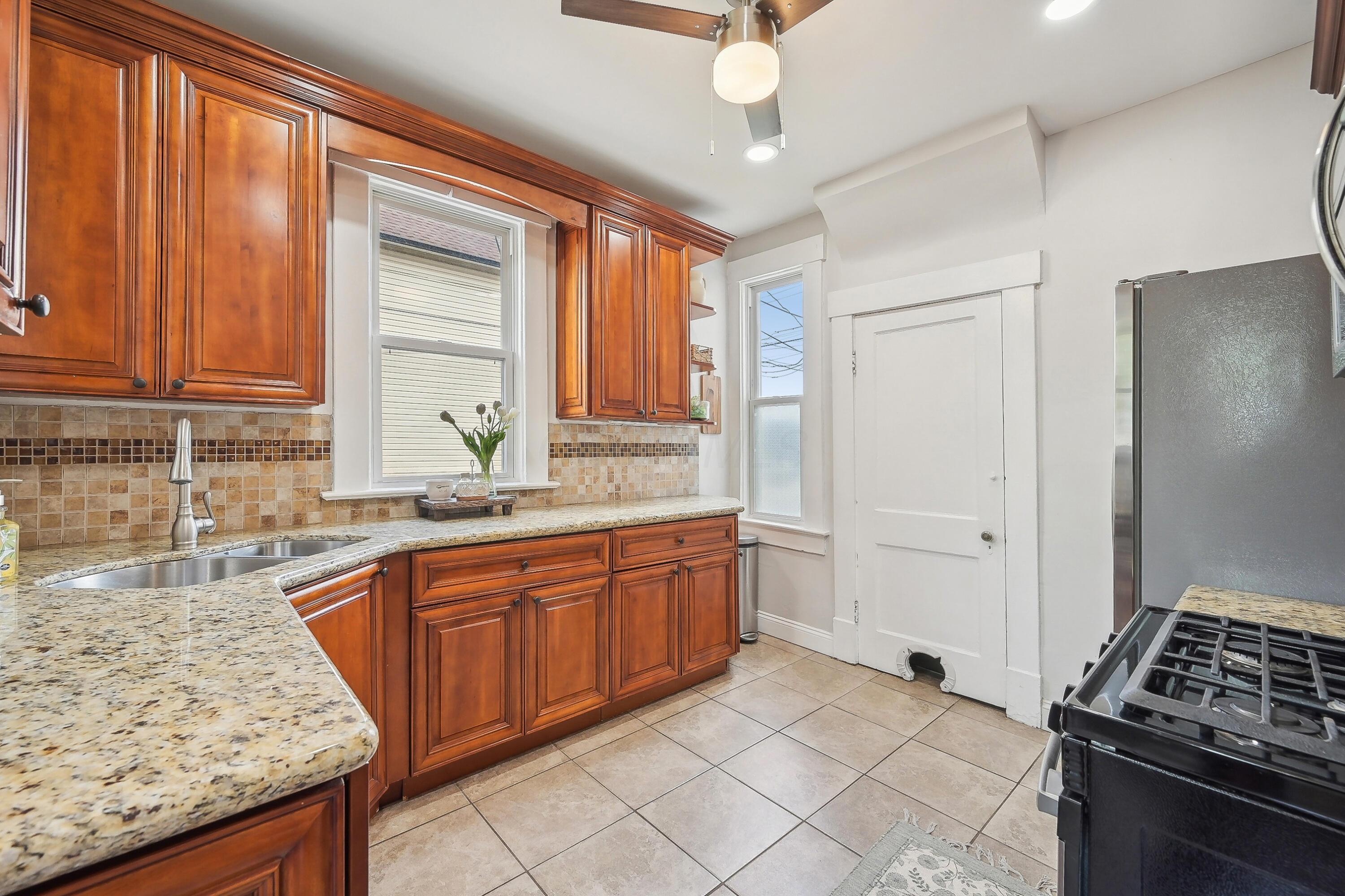 Kitchen with warm wood cabinets, granite counters, tiled backsplash, and a black range.