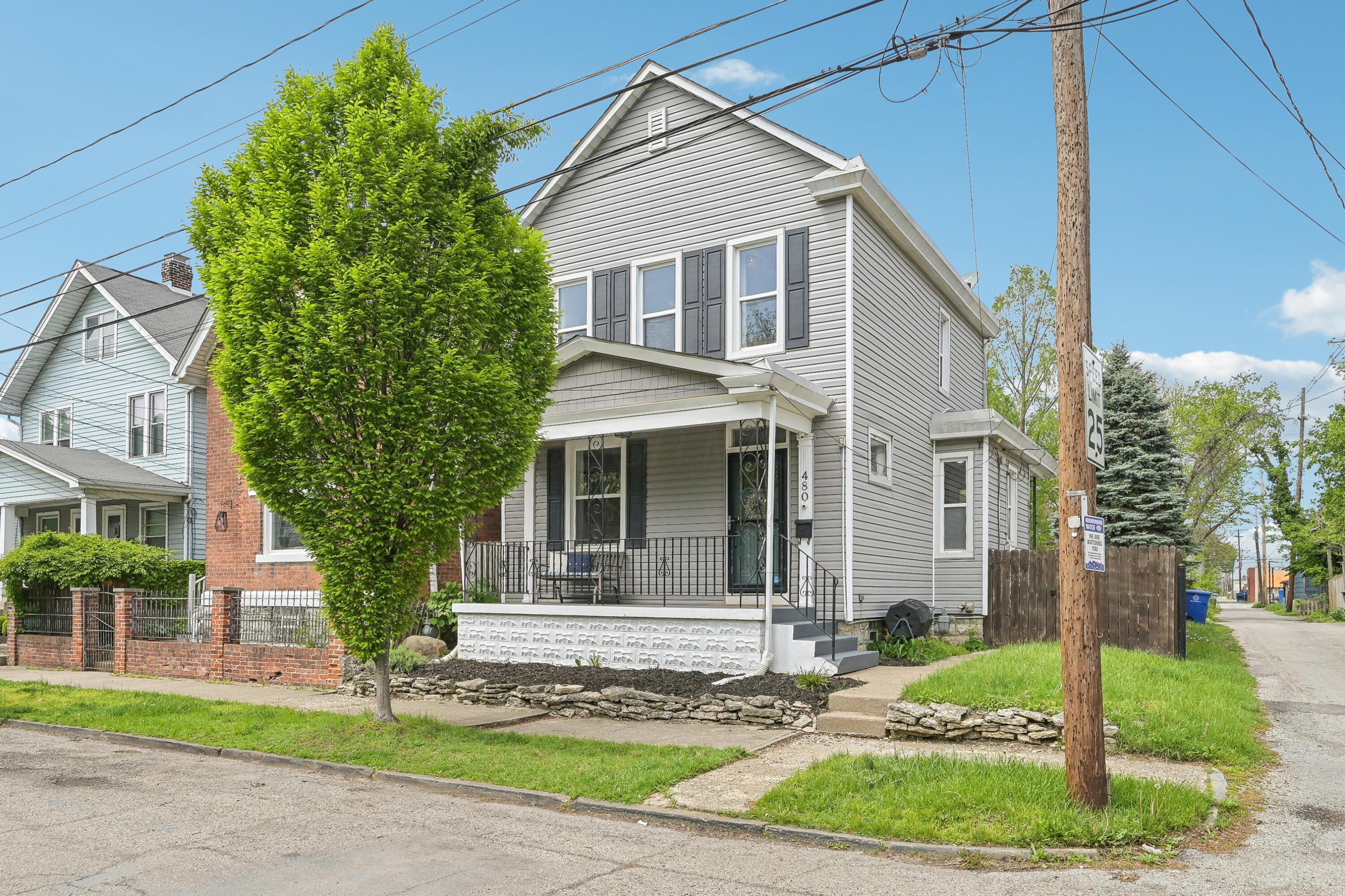 Two-story gray house with a covered porch and large leafy tree in front.