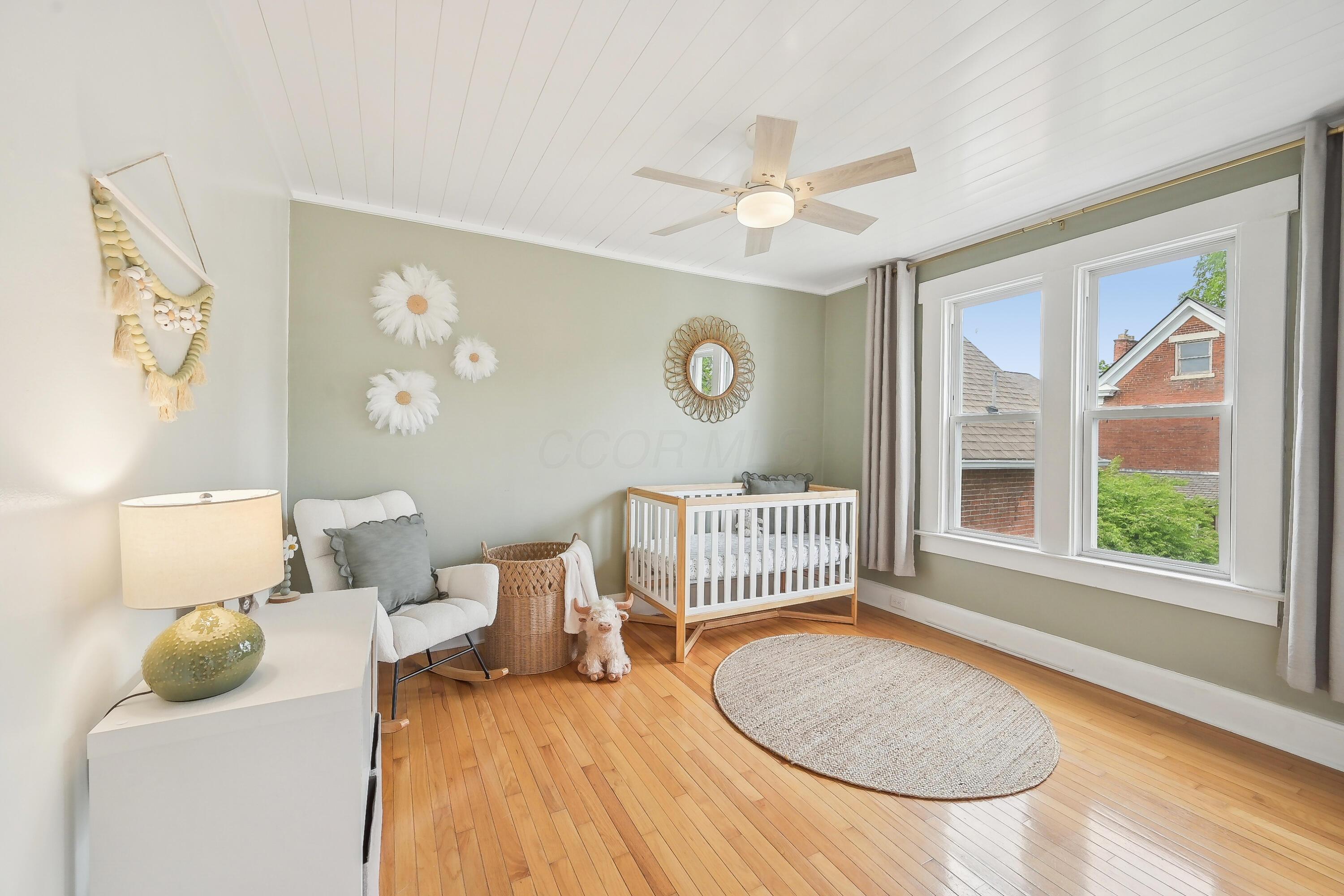 Staged nursery with a white and wood crib, rocking chair, and large windows.