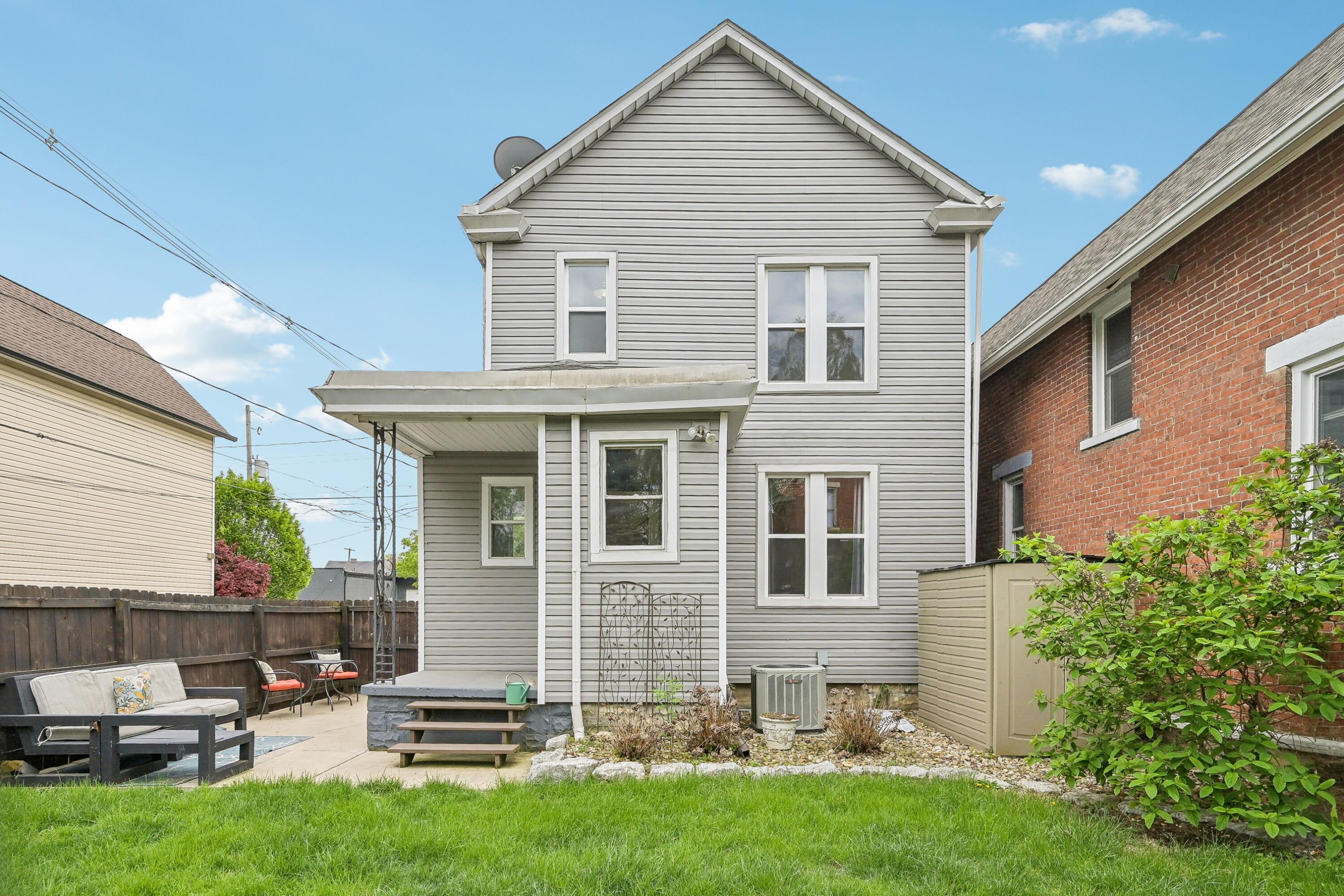 Rear of a gray-sided two-story house, with a fenced patio, outdoor seating, and lawn.