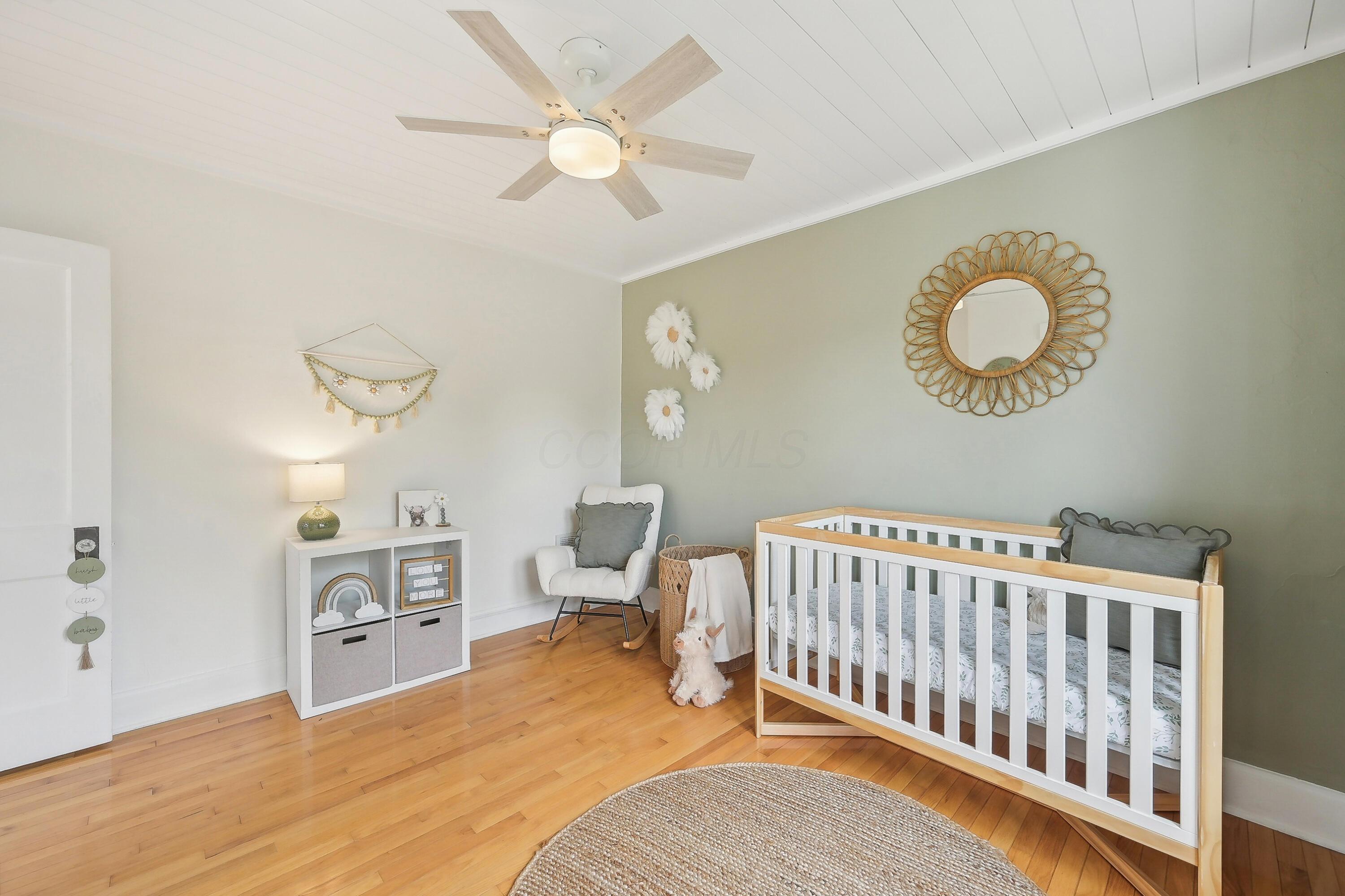 Staged nursery with a white crib, pale green accent wall, hardwood floors, and rocking chair.