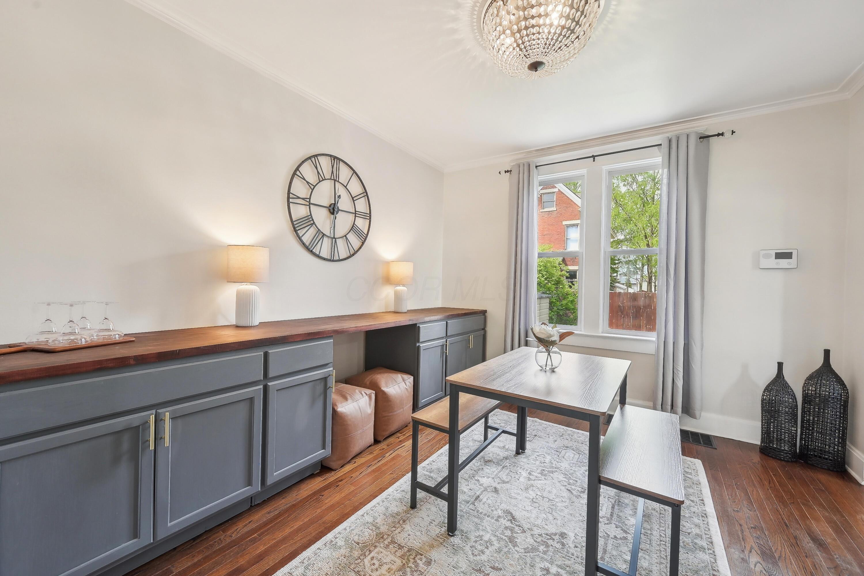 Dining room with gray built-ins, a wood dining table, patterned rug, and large curtained window.