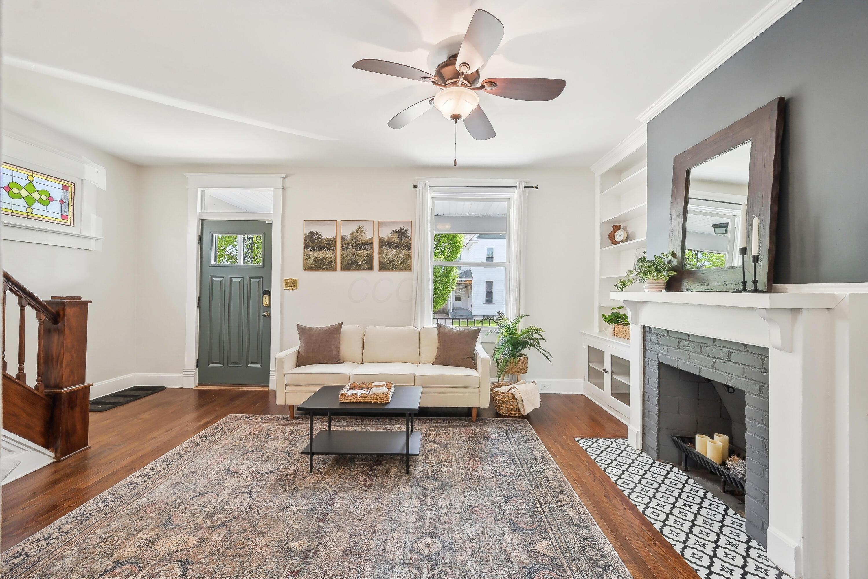 Living room with a cream sofa, gray brick fireplace, built-in shelves, and hardwood floors.