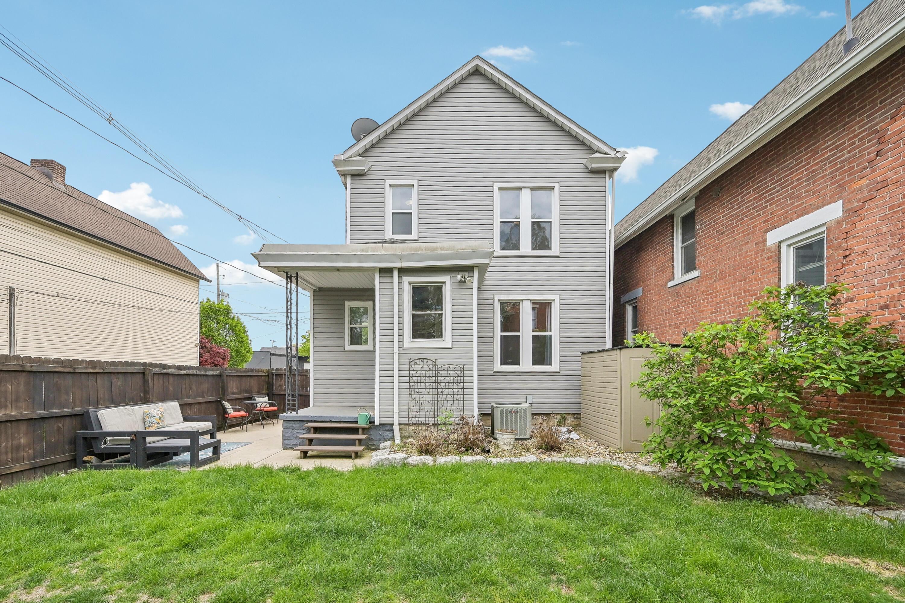 Rear of a gray-sided house with a fenced lawn and patio seating.