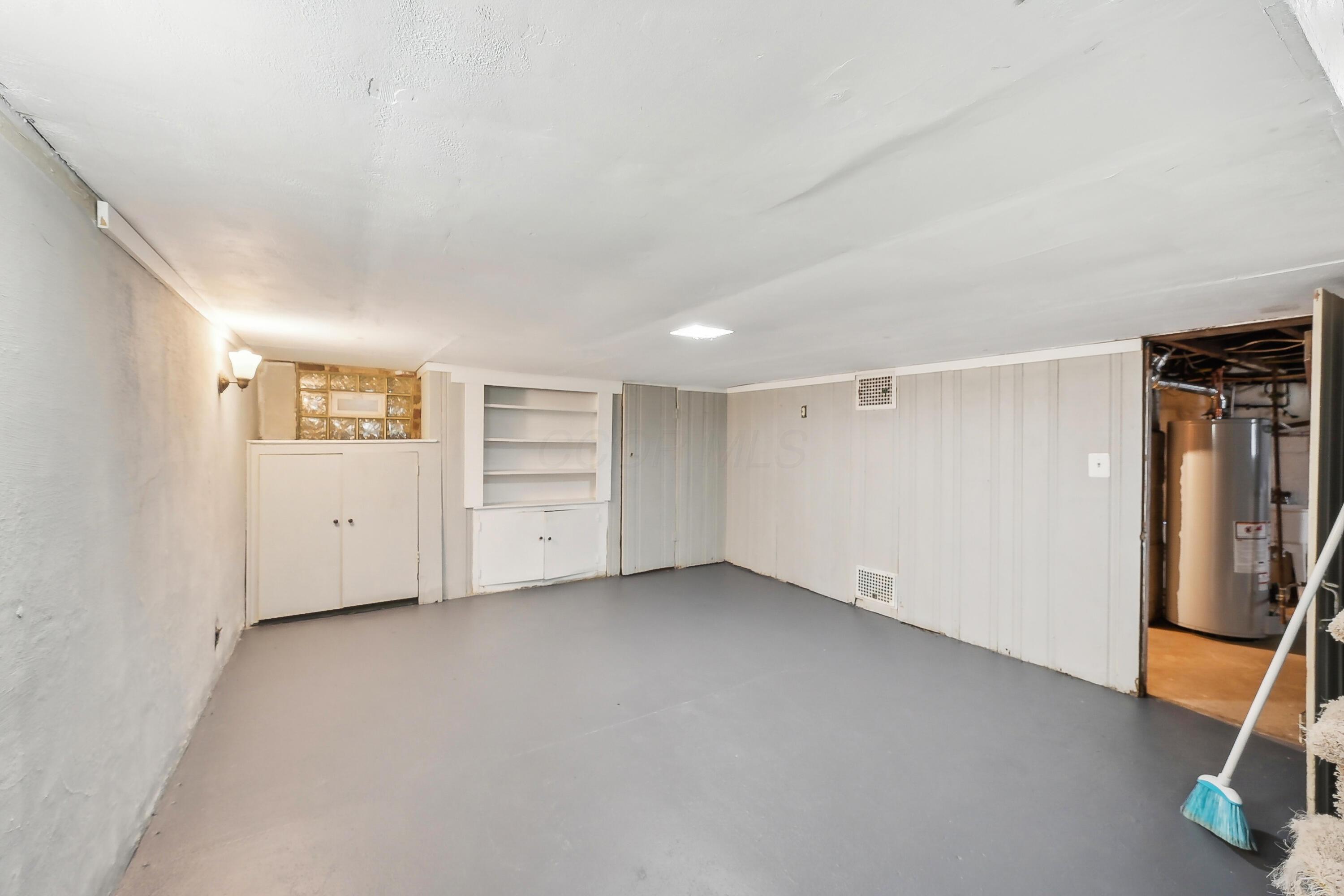 Empty basement room with built-in shelves and cabinets, opening into a utility area with a water heater.