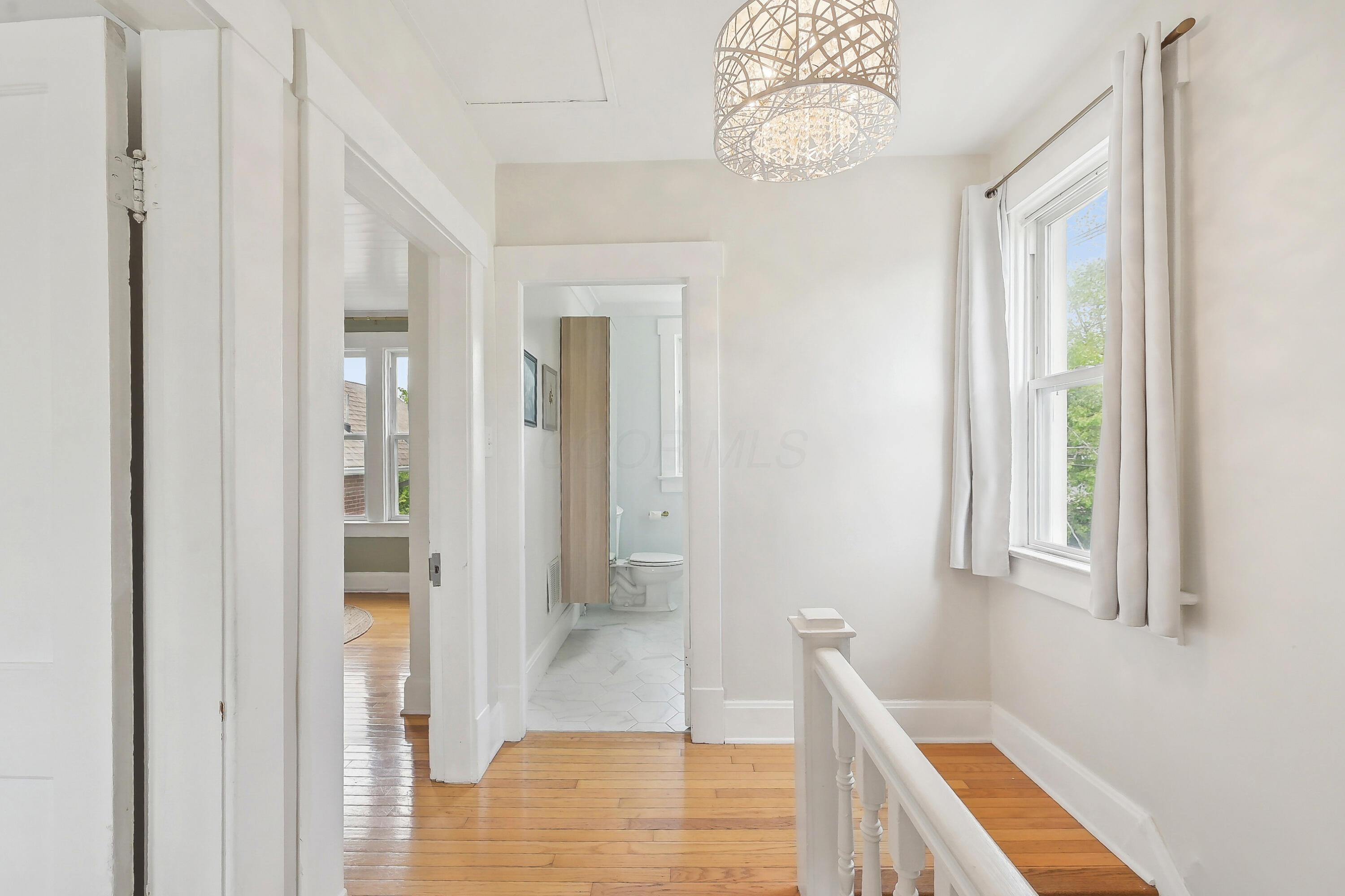 Upstairs landing with hardwood floors, a decorative pendant light, and a doorway to a tiled bathroom.