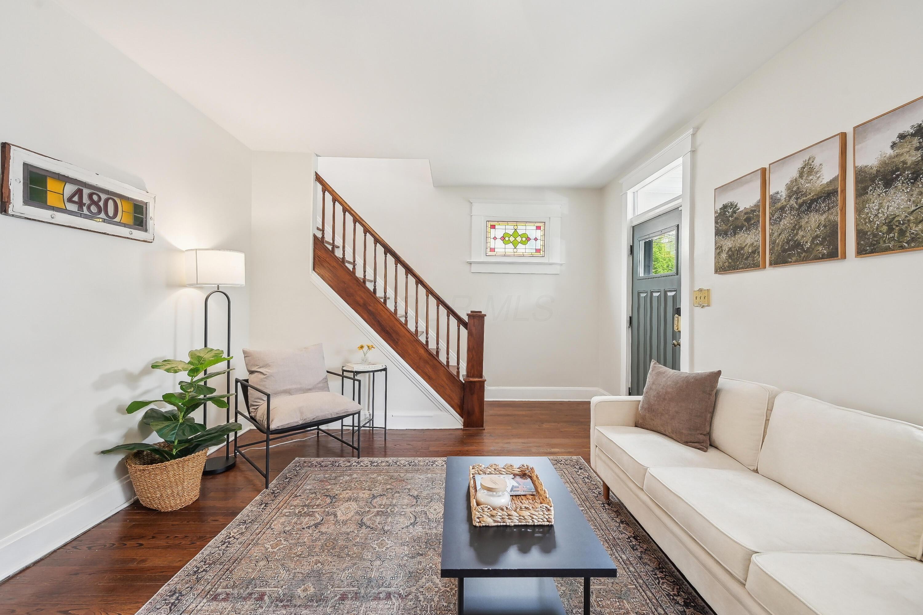 Staged living room with a dark wood staircase, hardwood floors, and stained-glass windows.