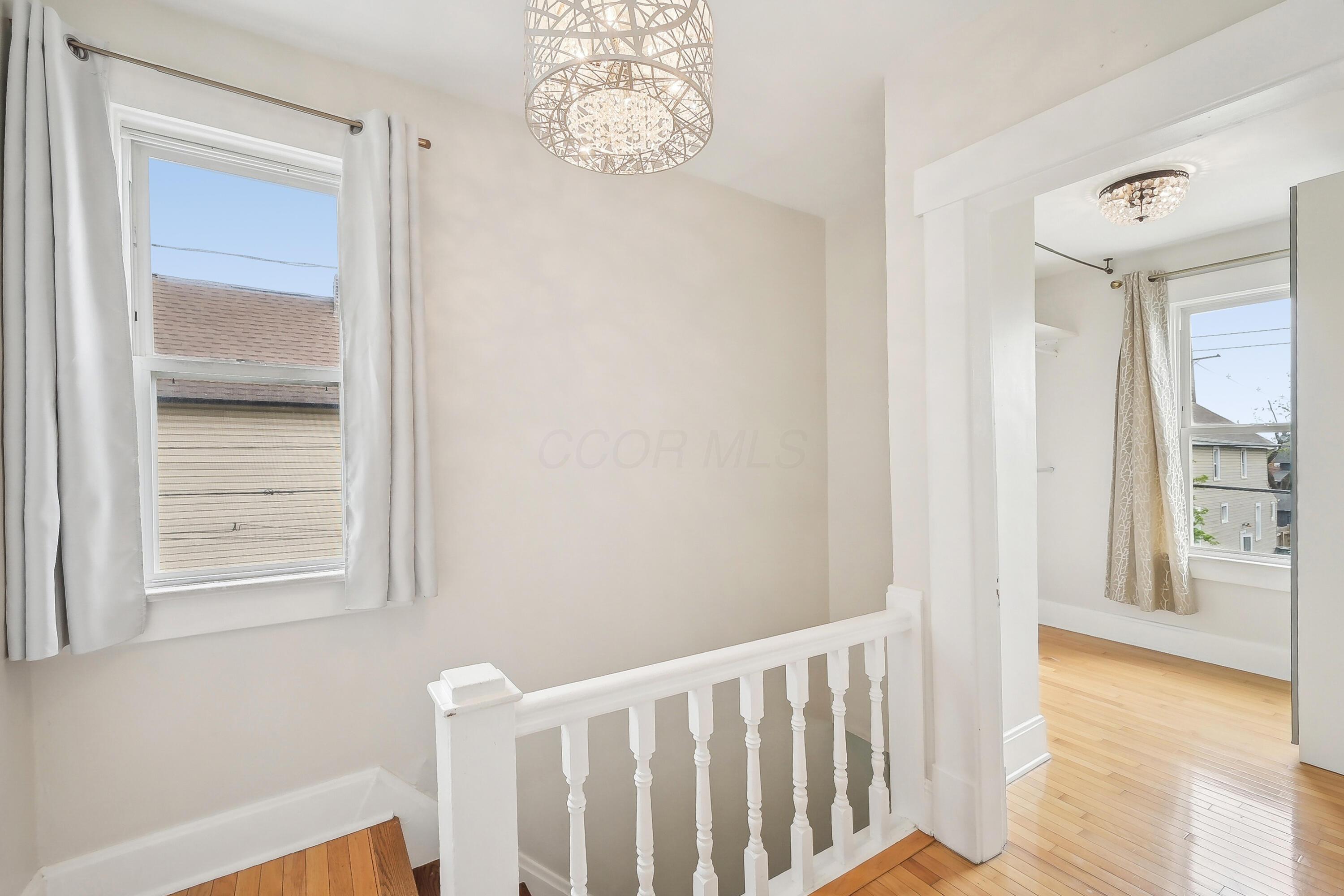 Upstairs landing with white balustrade, hardwood floors, tall windows, and decorative chandeliers.