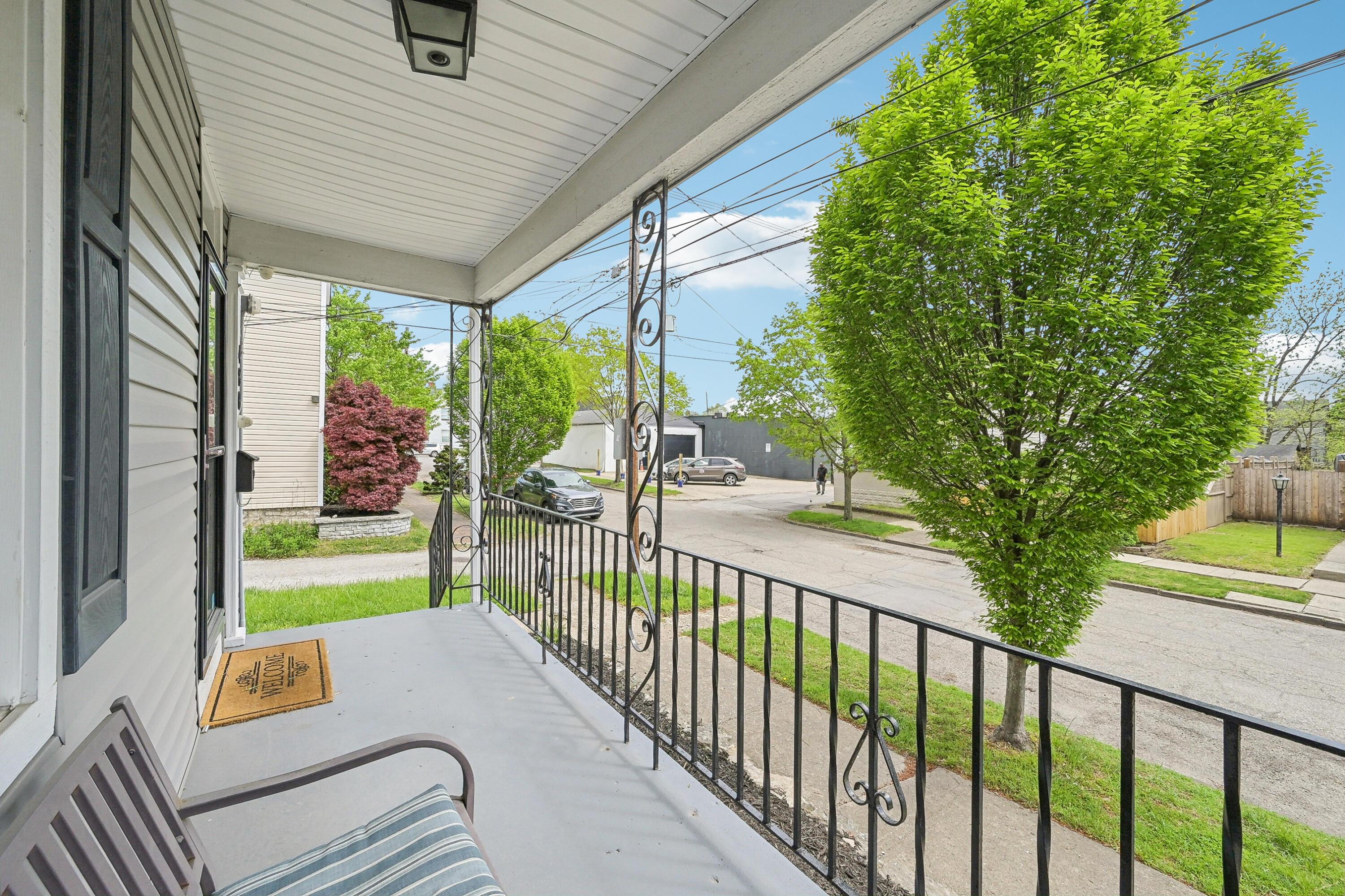 Covered front porch with decorative black railing overlooking a tree-lined residential street.