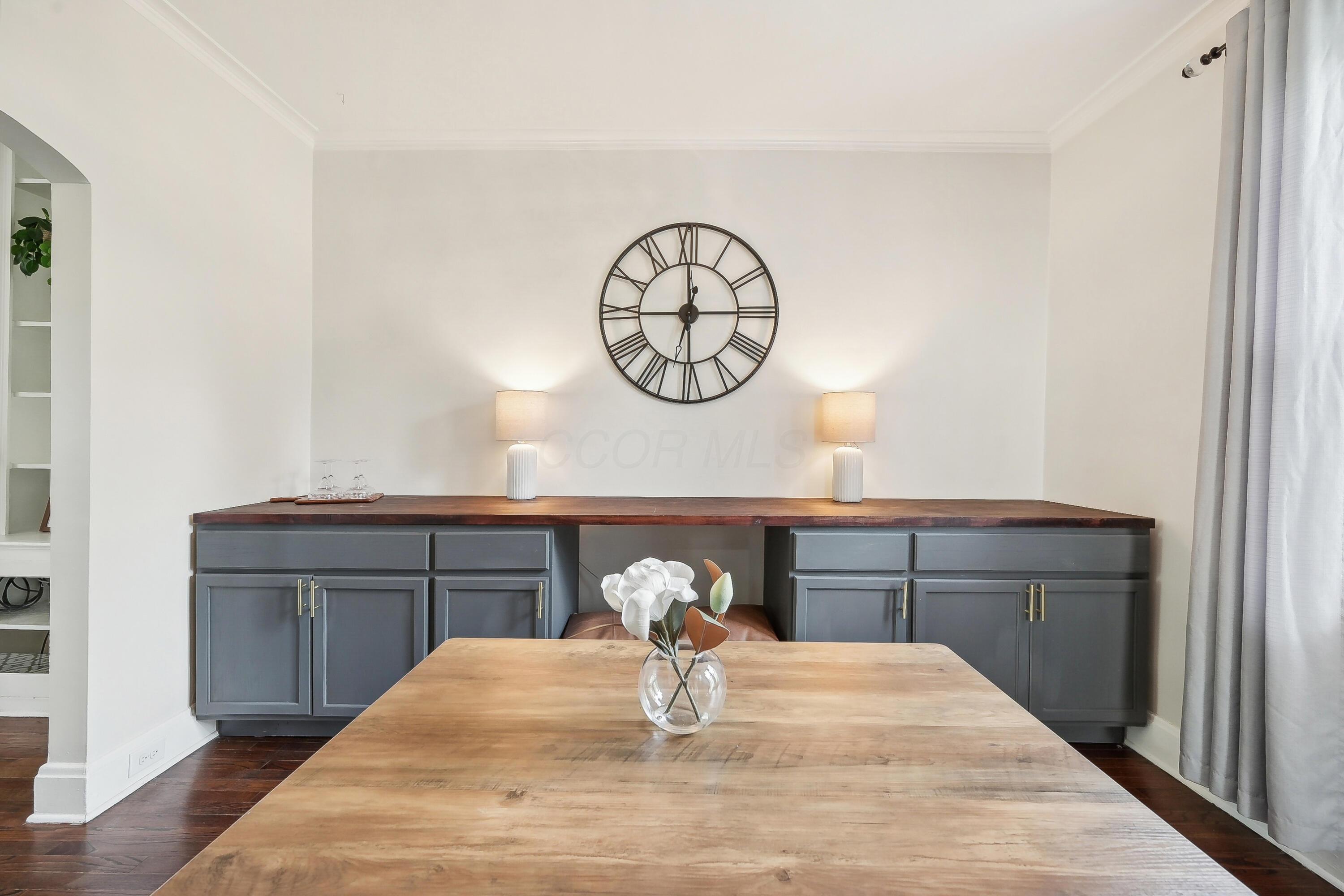 Dining room with a large wood table, dark built-in buffet, and oversized wall clock.