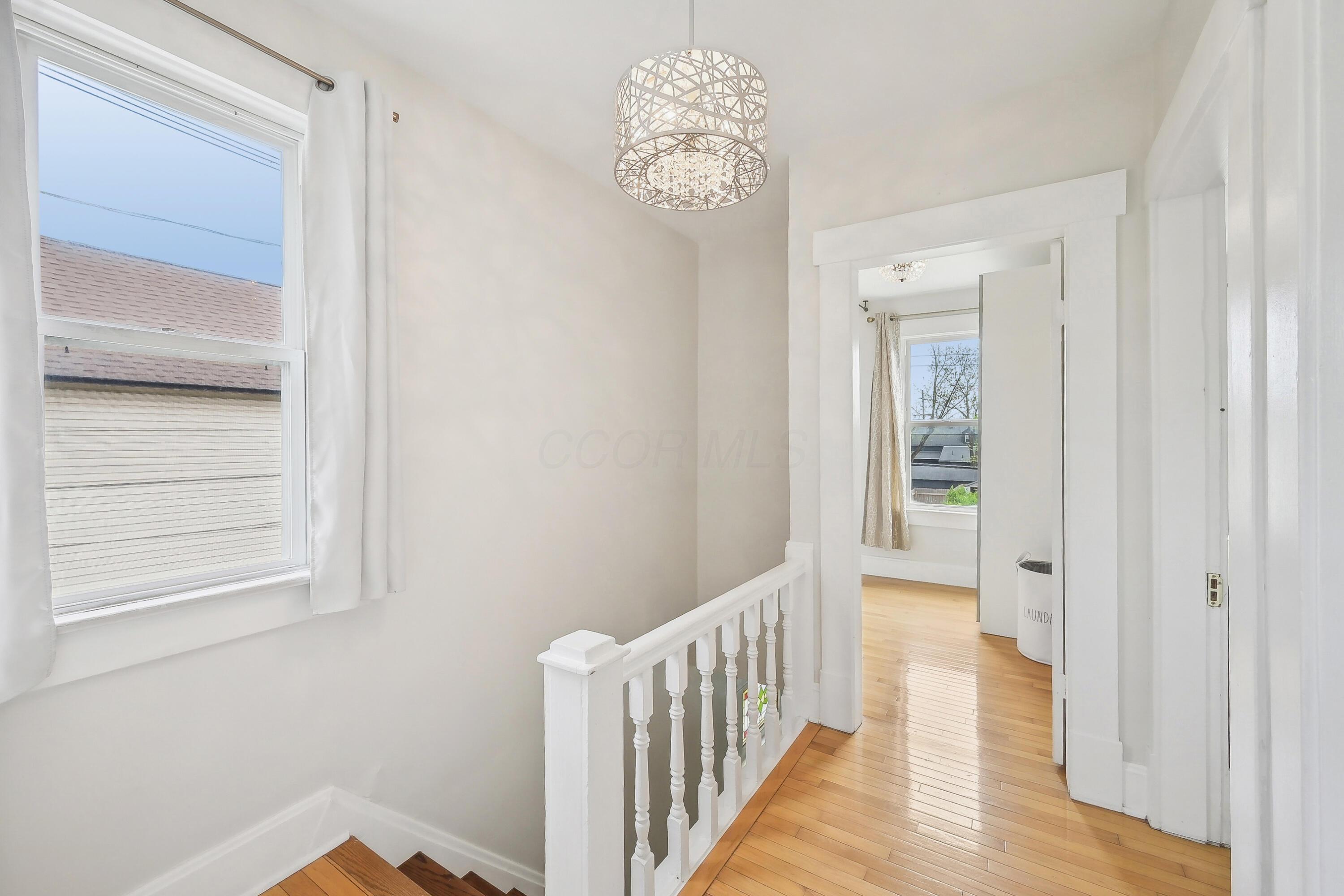 Upstairs hallway with hardwood floors, white stair railing, large window, and decorative ceiling light.