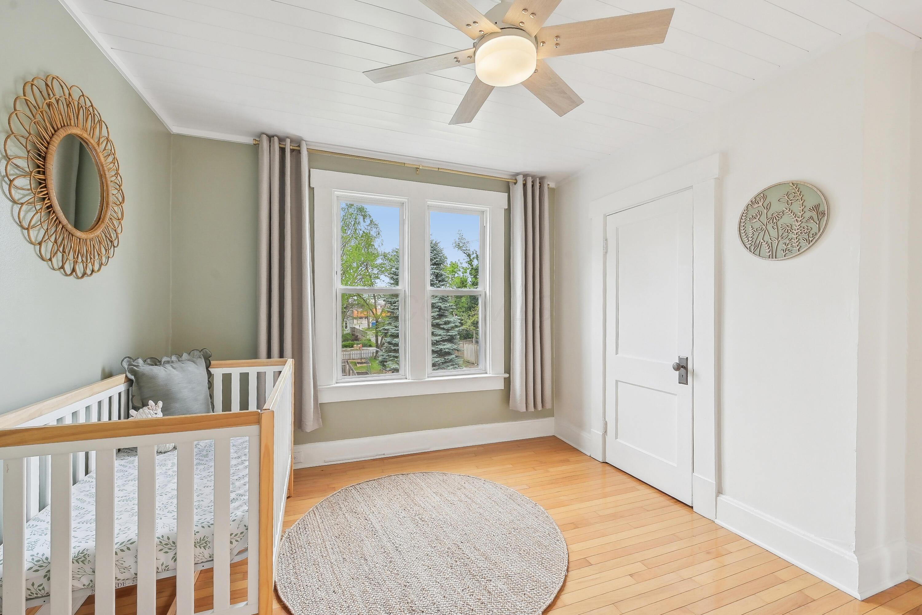Bright nursery with a white-and-wood crib, two curtained windows, and hardwood floors.
