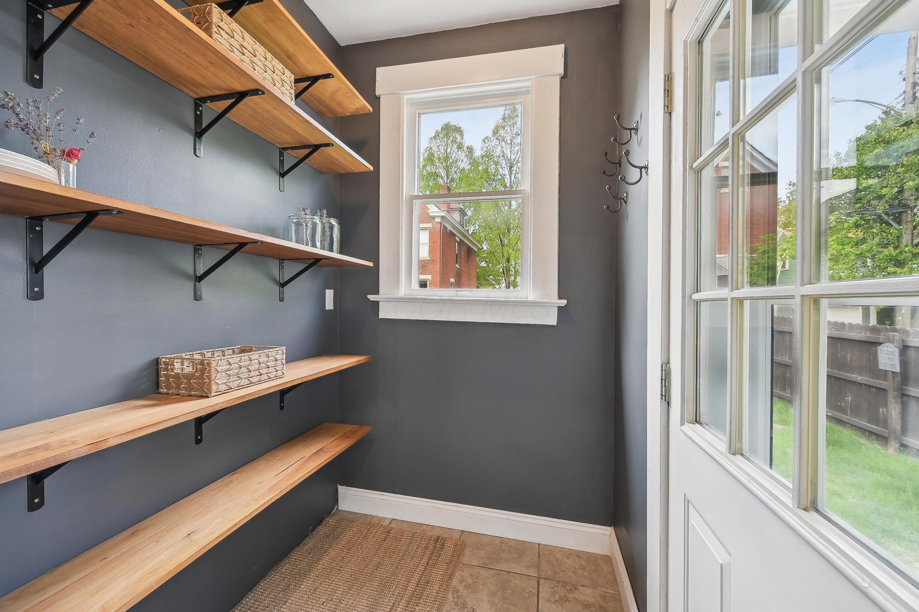 Mudroom with long wooden shelves, coat hooks, and a glazed white door.