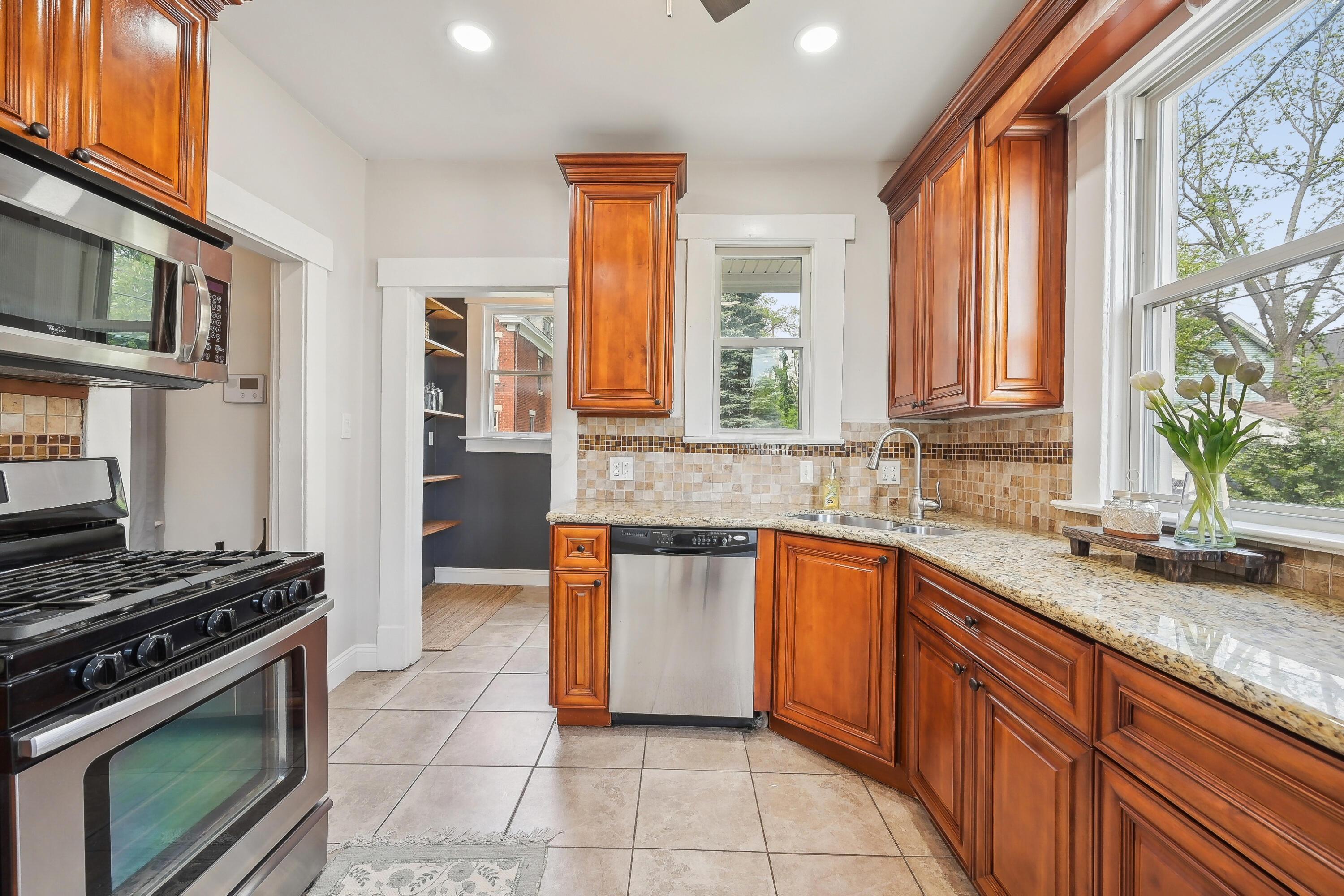 Kitchen with warm wood cabinetry, granite counters, tiled backsplash, and large windows above the sink.