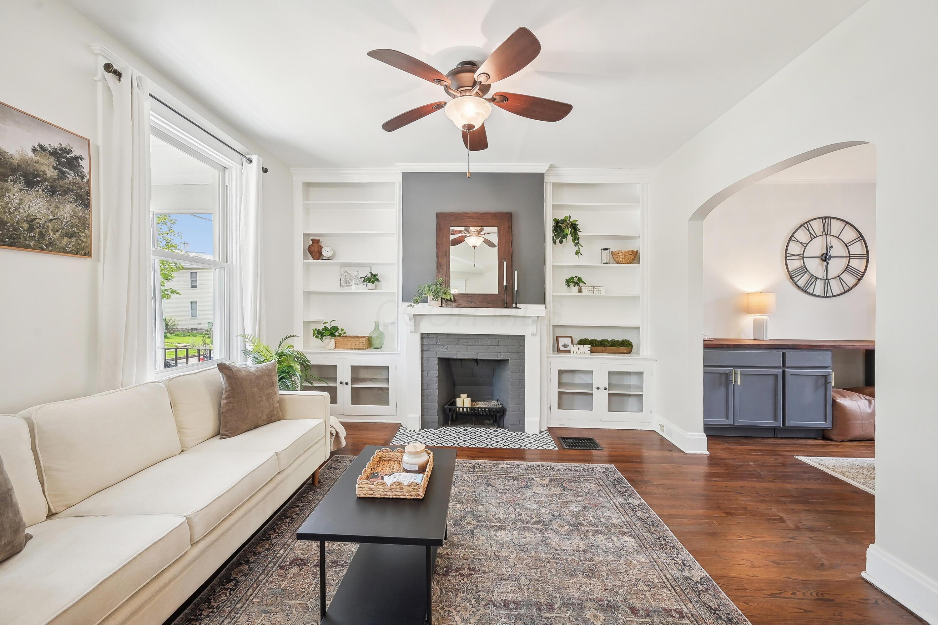 Staged living room with a gray-brick fireplace, white built-in shelves, and an arched opening.