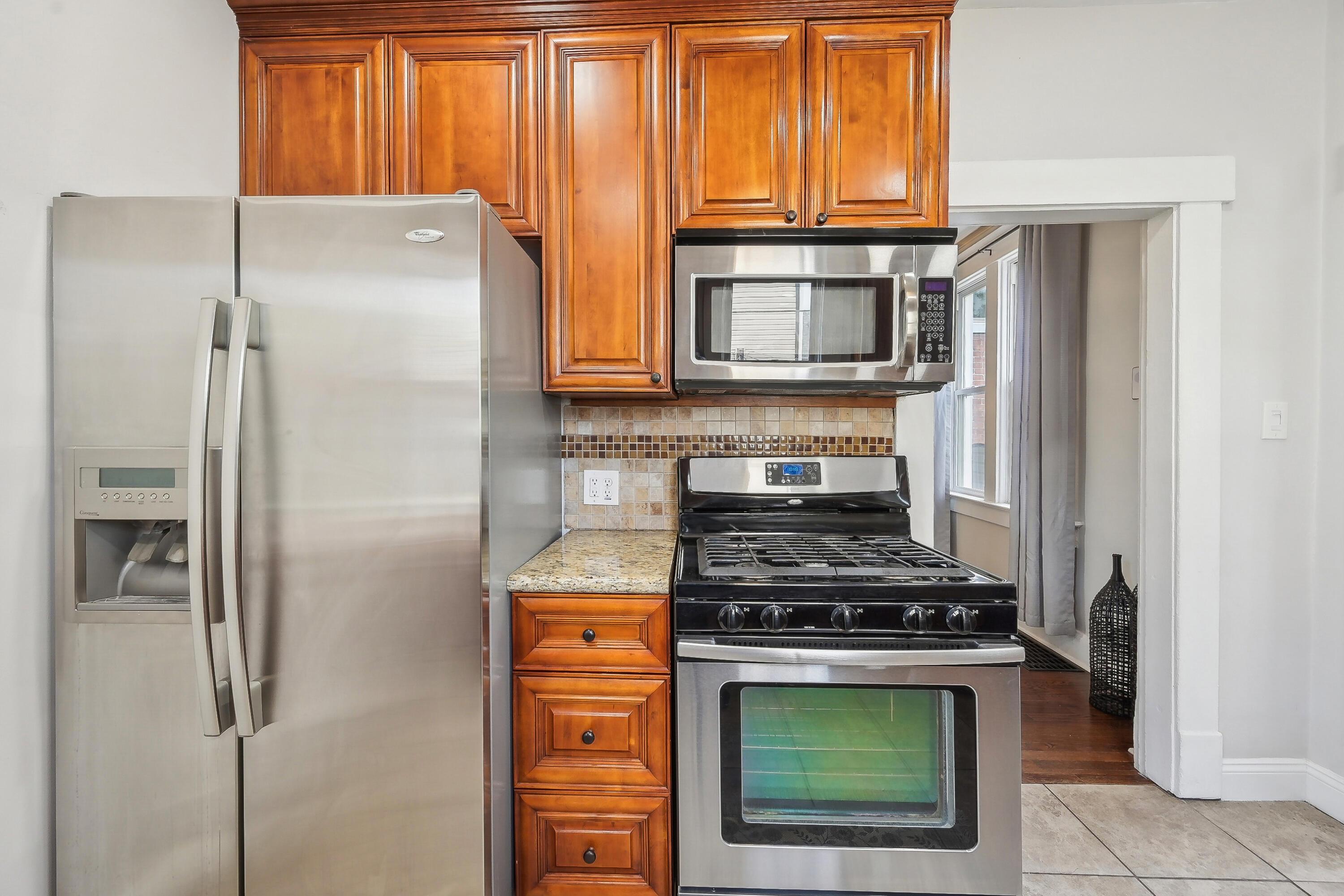 Kitchen with rich wood cabinets, stainless refrigerator, and gas range beneath a microwave.