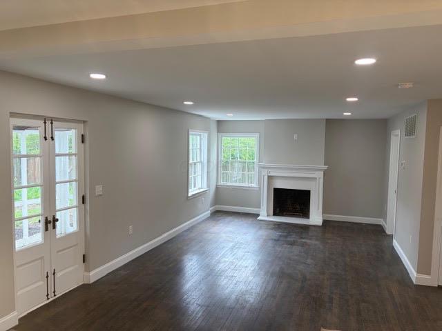 Empty living room with dark hardwood floors, a white fireplace, and French doors.