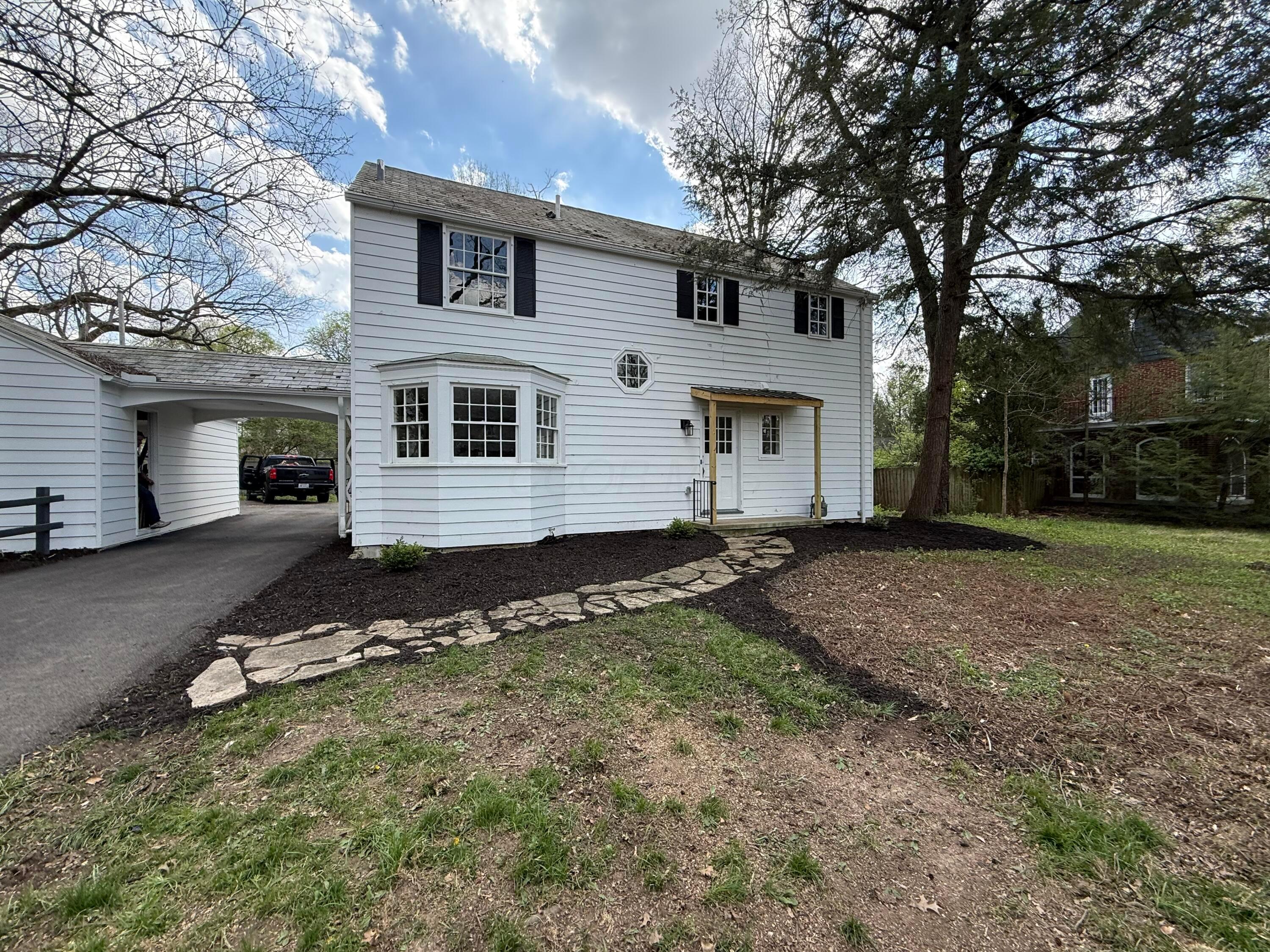 White two-story house with a bay window, attached carport, and stone walkway across the front yard.